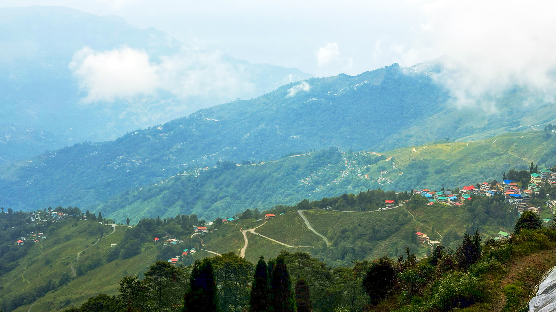 Cloudy mountain landscape with green hills and a village of colorful houses.