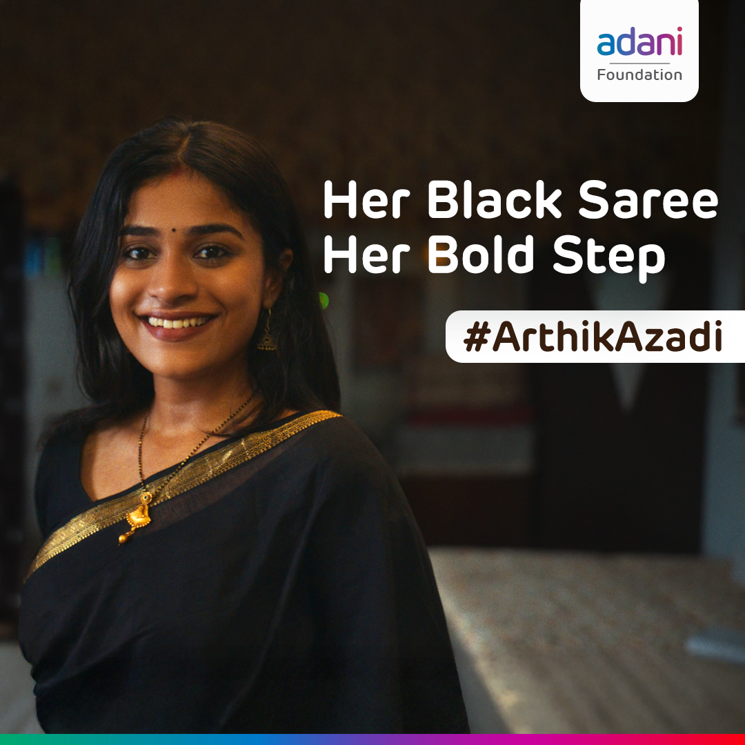 Smiling woman in black saree with gold border and mangalsutra. Text: "Her Black Saree Her Bold Step #ArthikAzadi".