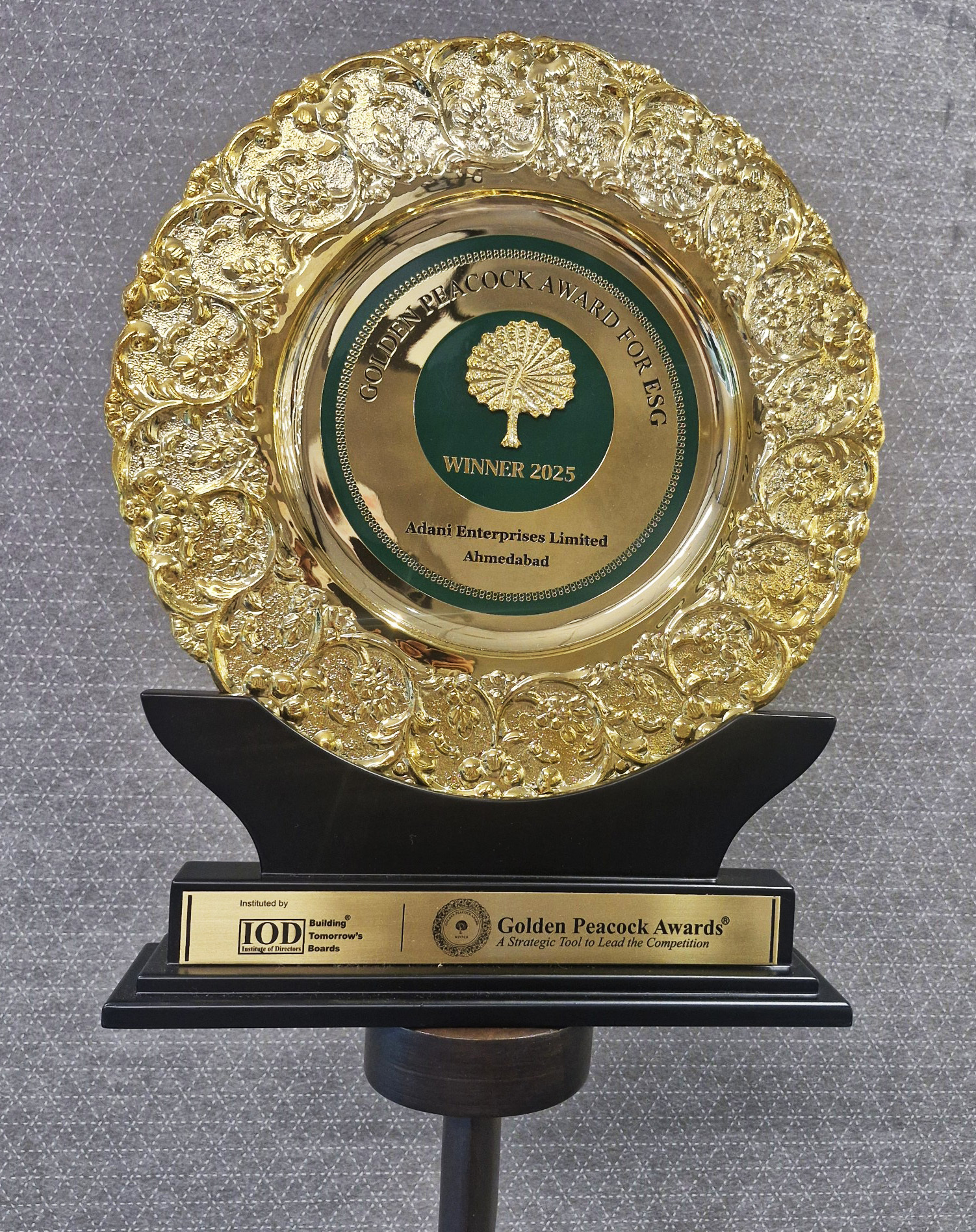 A gold and green Golden Peacock Award plaque for ESG, Winner 2025, Adani Enterprises Limited.