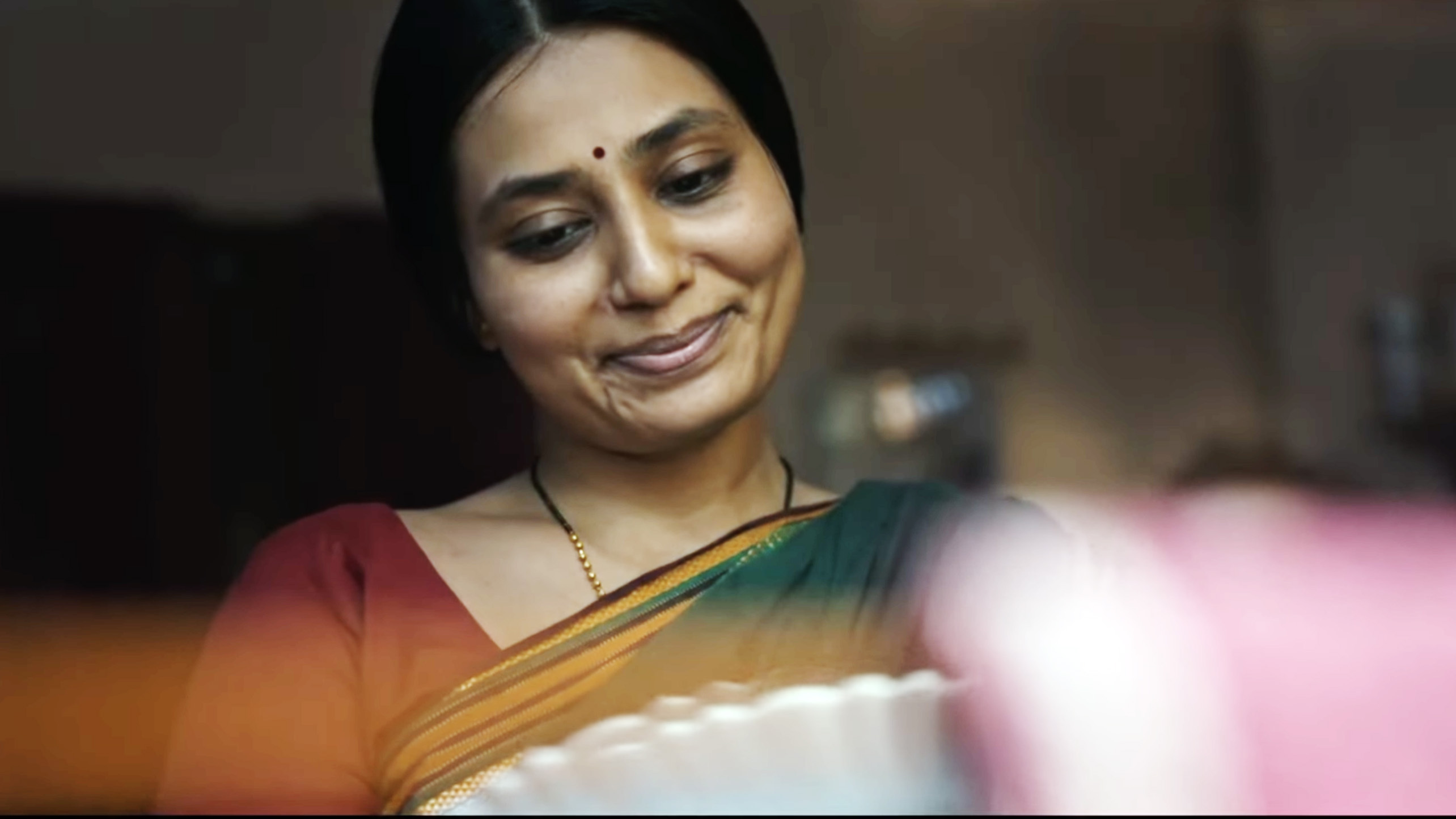 Smiling woman in a saree with a bindi, looking down gently.