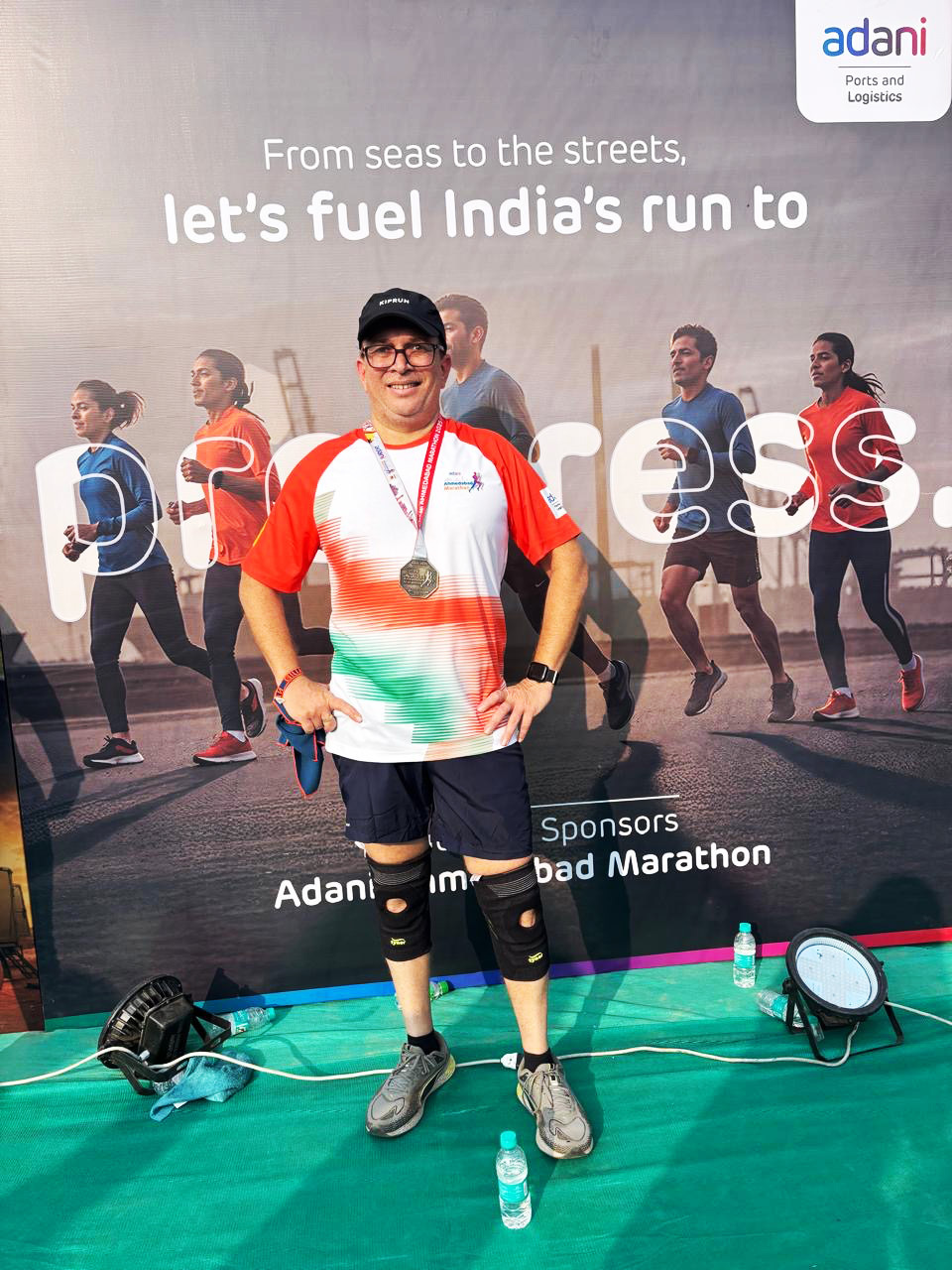 Man in running gear with medal stands proudly before an Adani marathon backdrop.