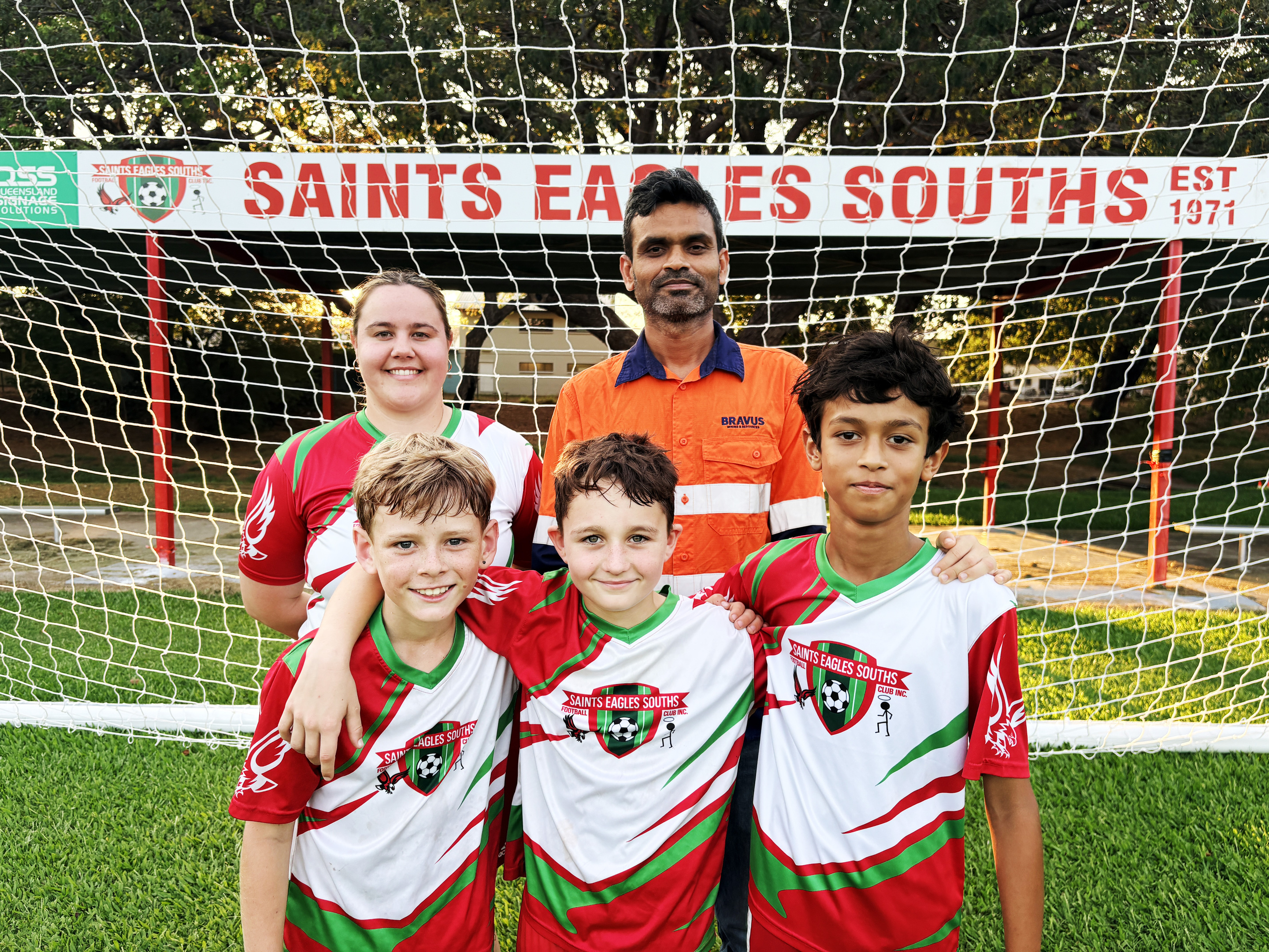 A group of five, including three boys in Saints Eagles Souths soccer jerseys, in front of a goal.