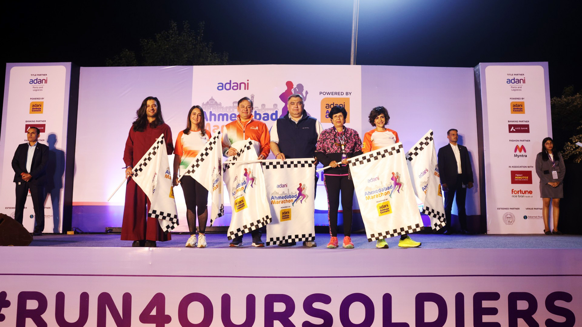 Group holding flags on stage at the Adani Ahmedabad Marathon event. #RUN4OURSOLDIERS.