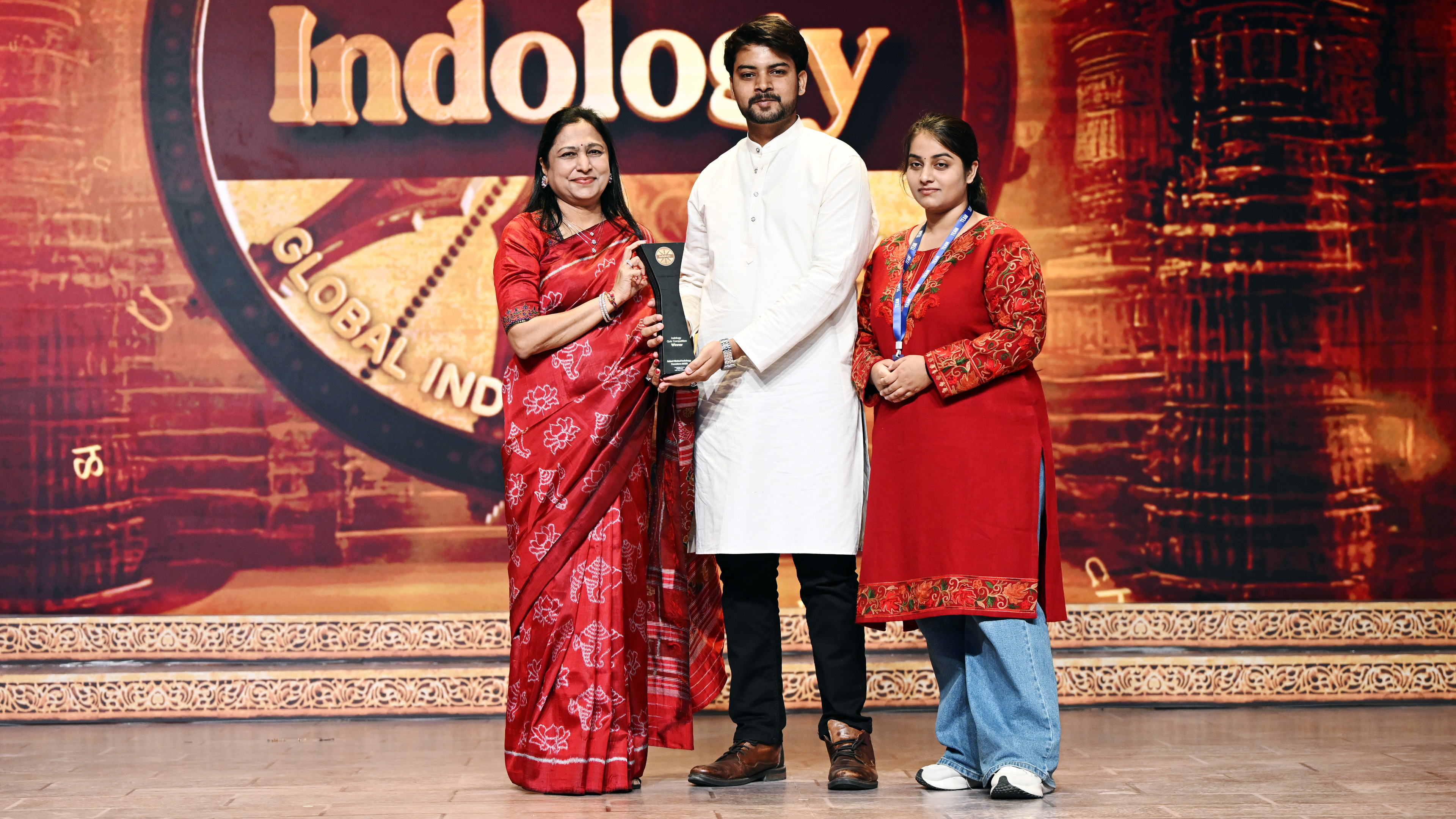 Three people on stage receive an award at an "Indology" event.