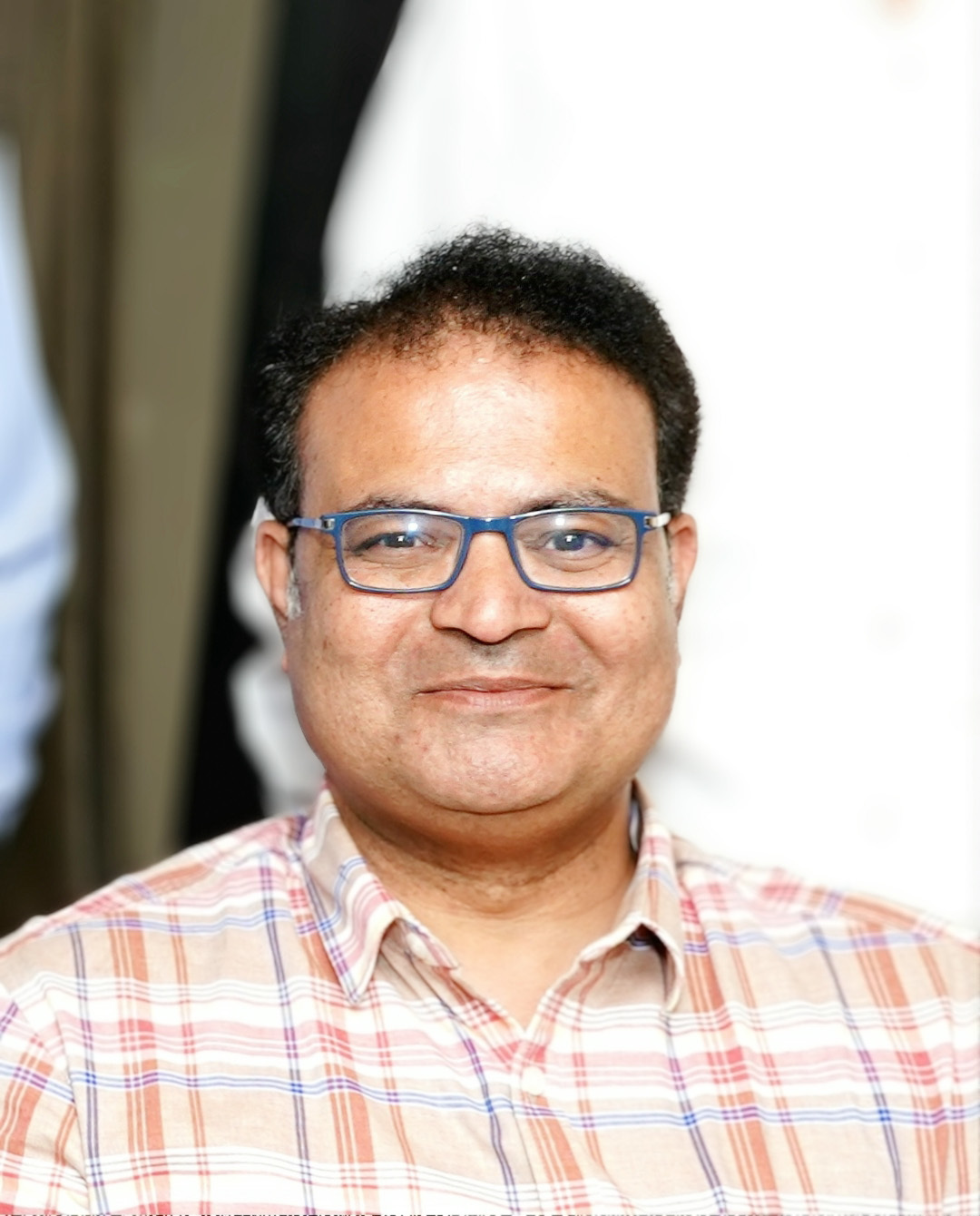 Smiling man with glasses in a plaid shirt.