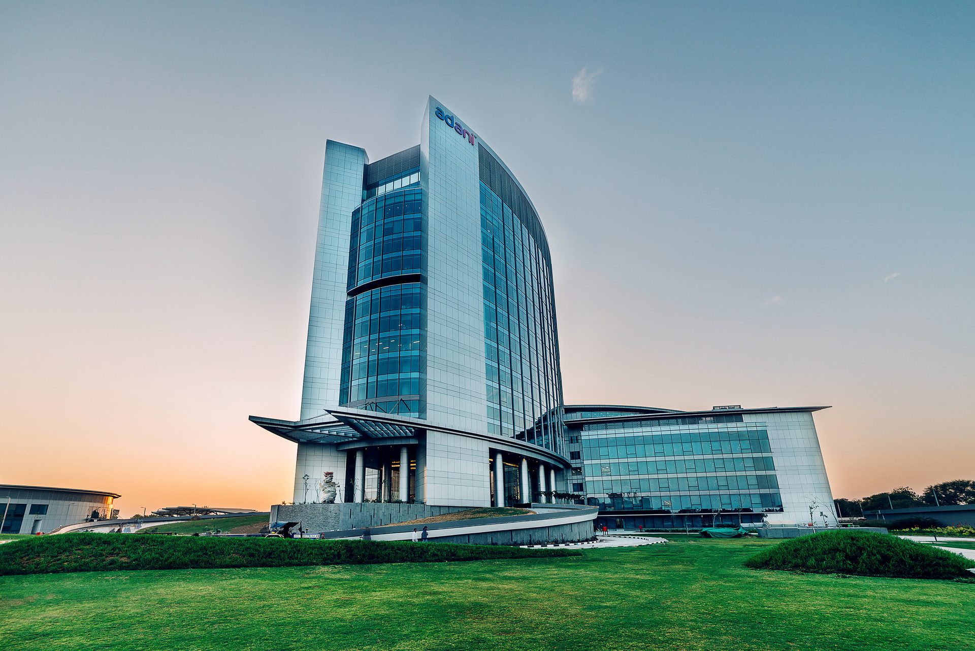 Modern Adani office building with green lawn at sunset.