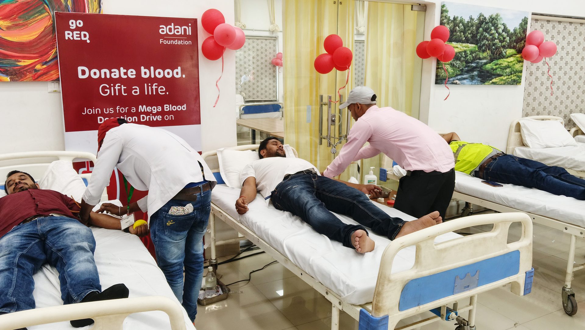 Adani Foundation's 'Go Red' blood drive: men donate, a banner reads 'Donate blood. Gift a life.'