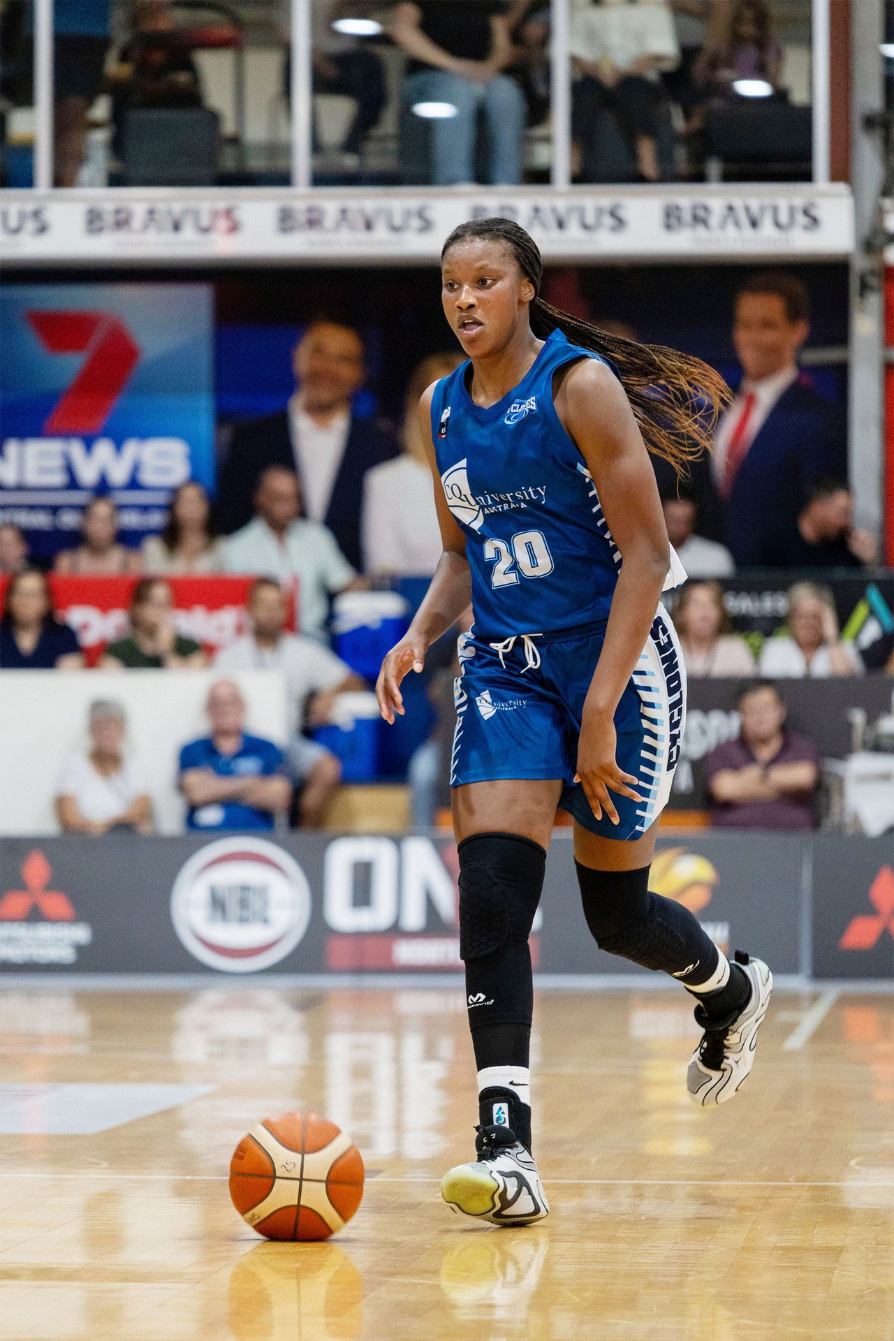 A female basketball player in a blue jersey dribbles a ball on a court.