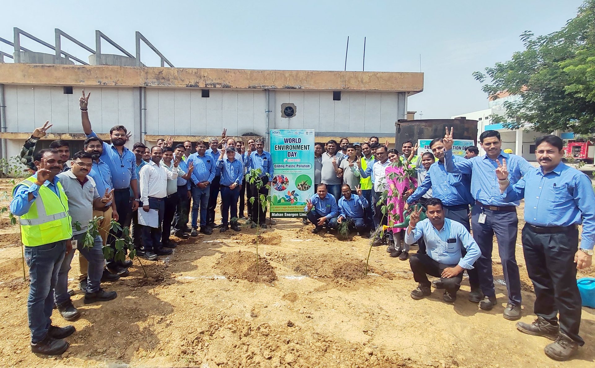 A diverse group of people planting saplings for World Environment Day, with a banner about plastic pollution.