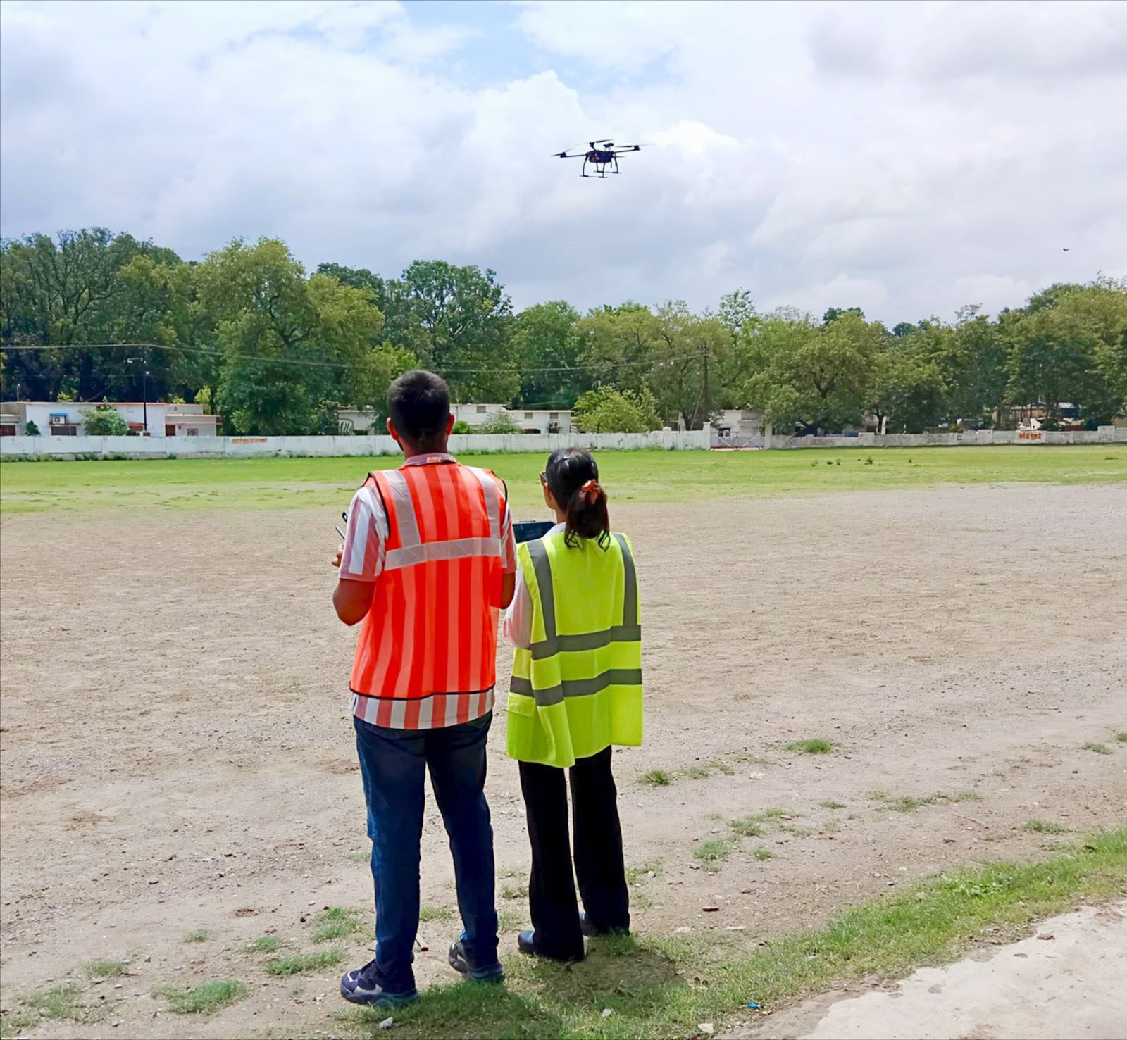Drone operators in safety vests flying a drone in a field.