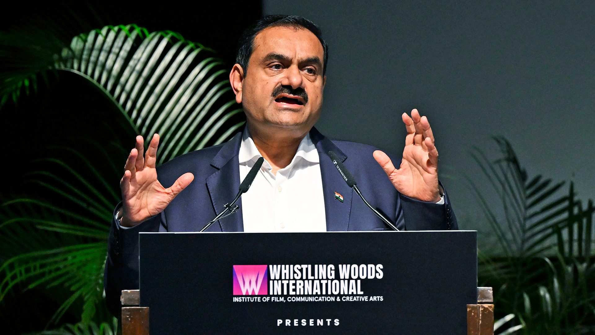 Gautam Adani speaks at a Whistling Woods International event, gesturing with his hands.