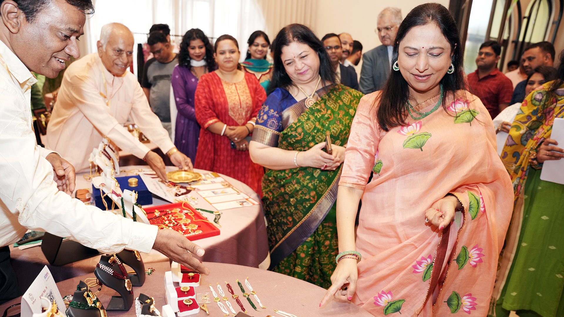 People, mainly women, browse and point at jewelry displayed on tables.