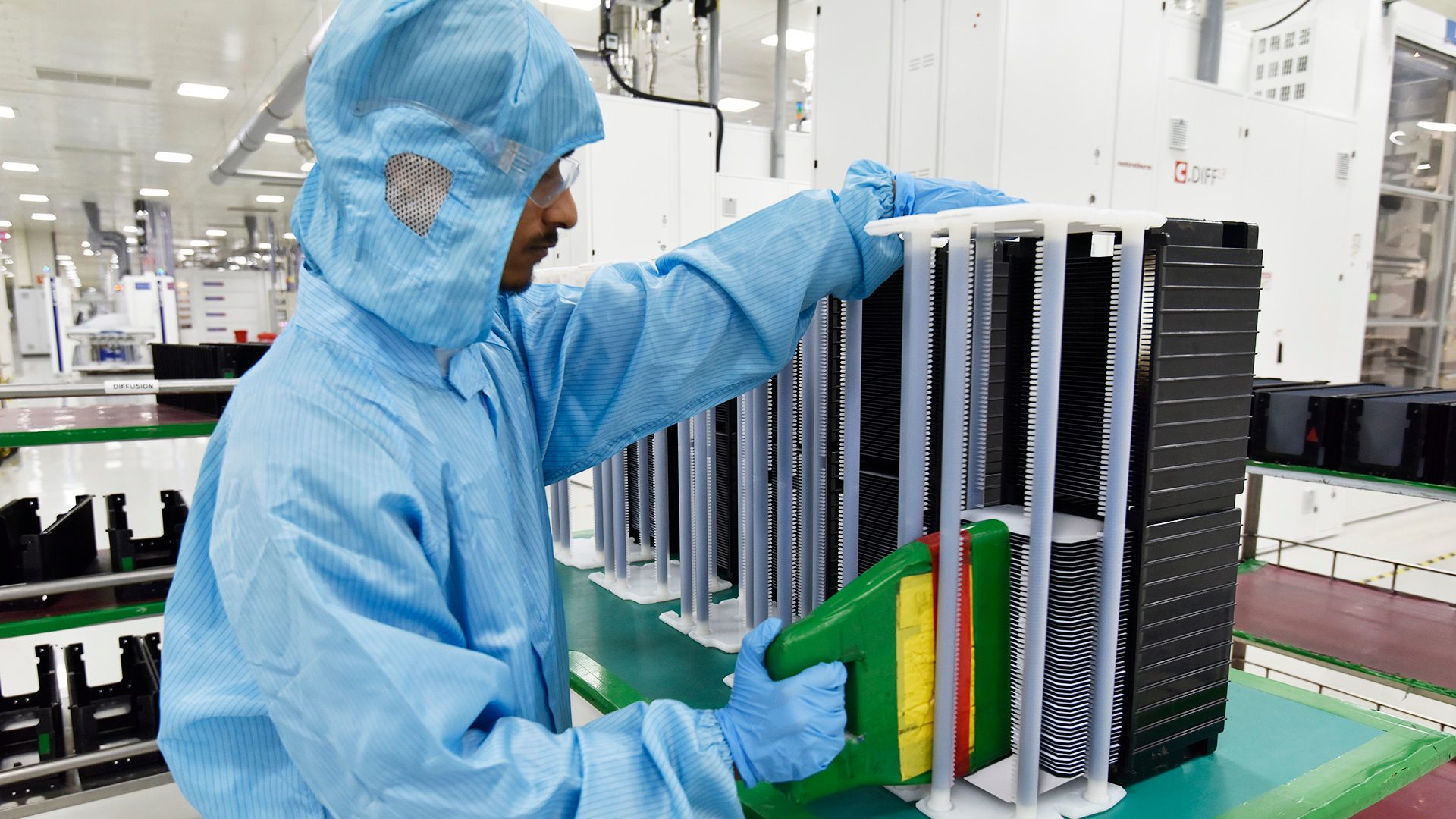 Tech worker in cleanroom suit placing components into a rack.