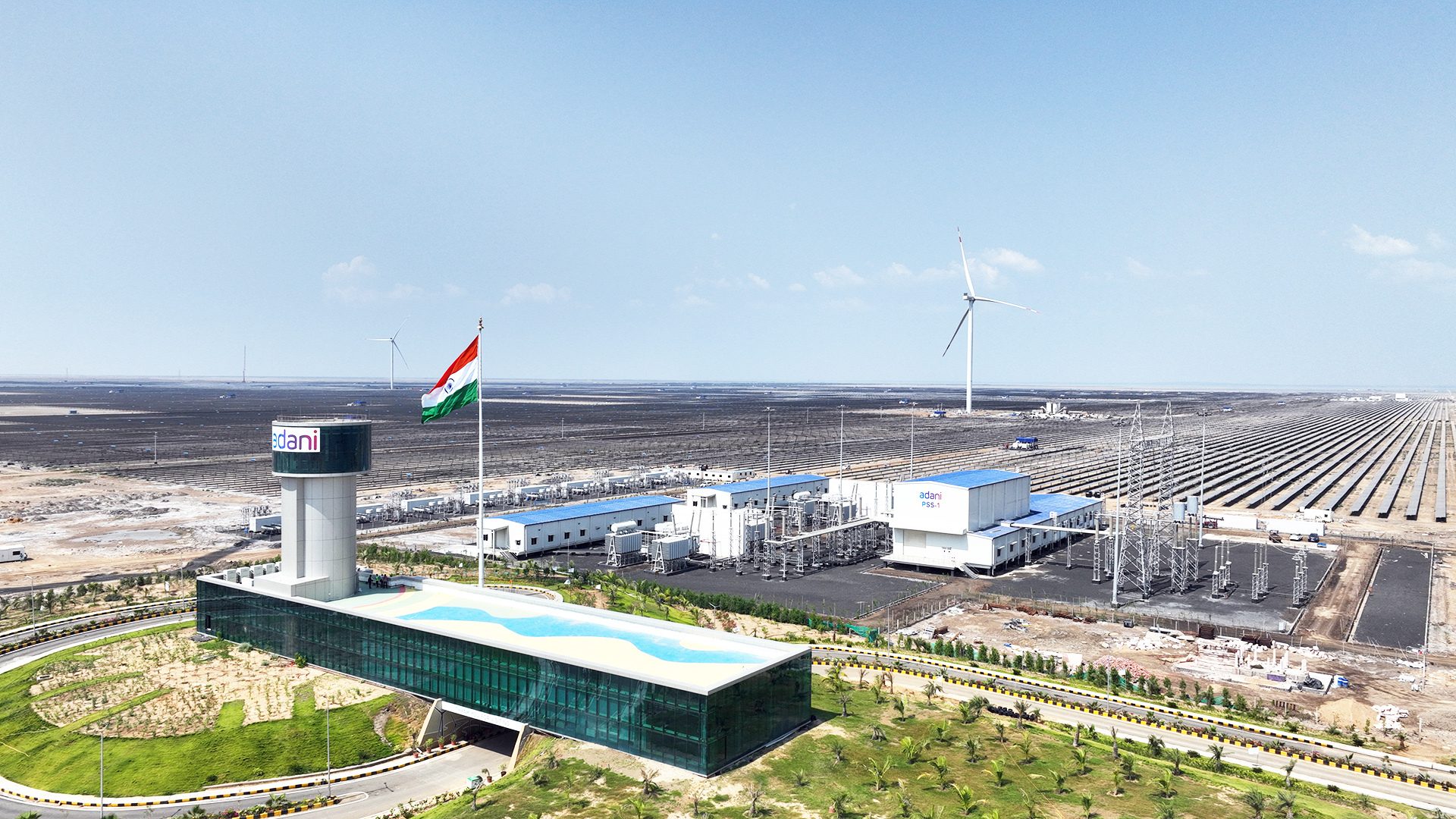 Adani's vast solar and wind energy park with facility, water tower, and Indian flag.