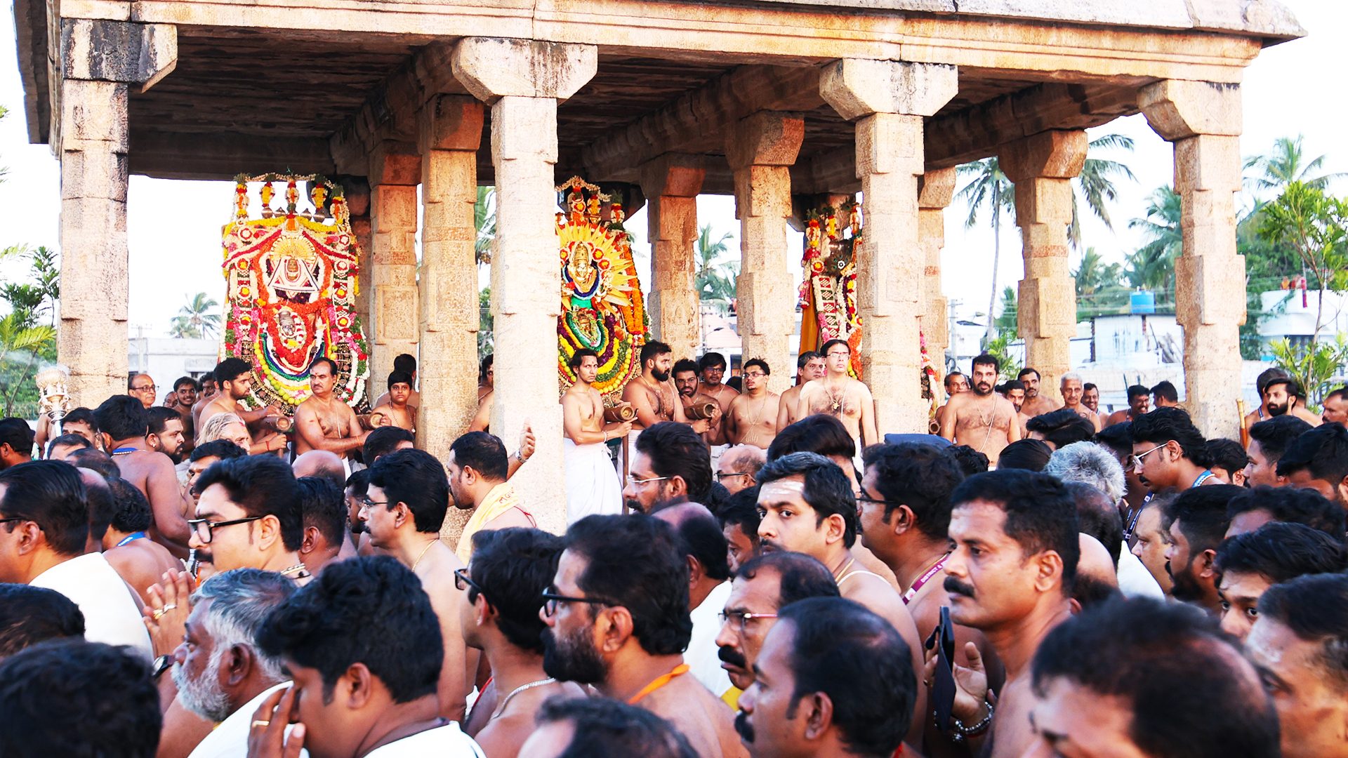 Devotees gather around ornate deities in an open-air temple.
