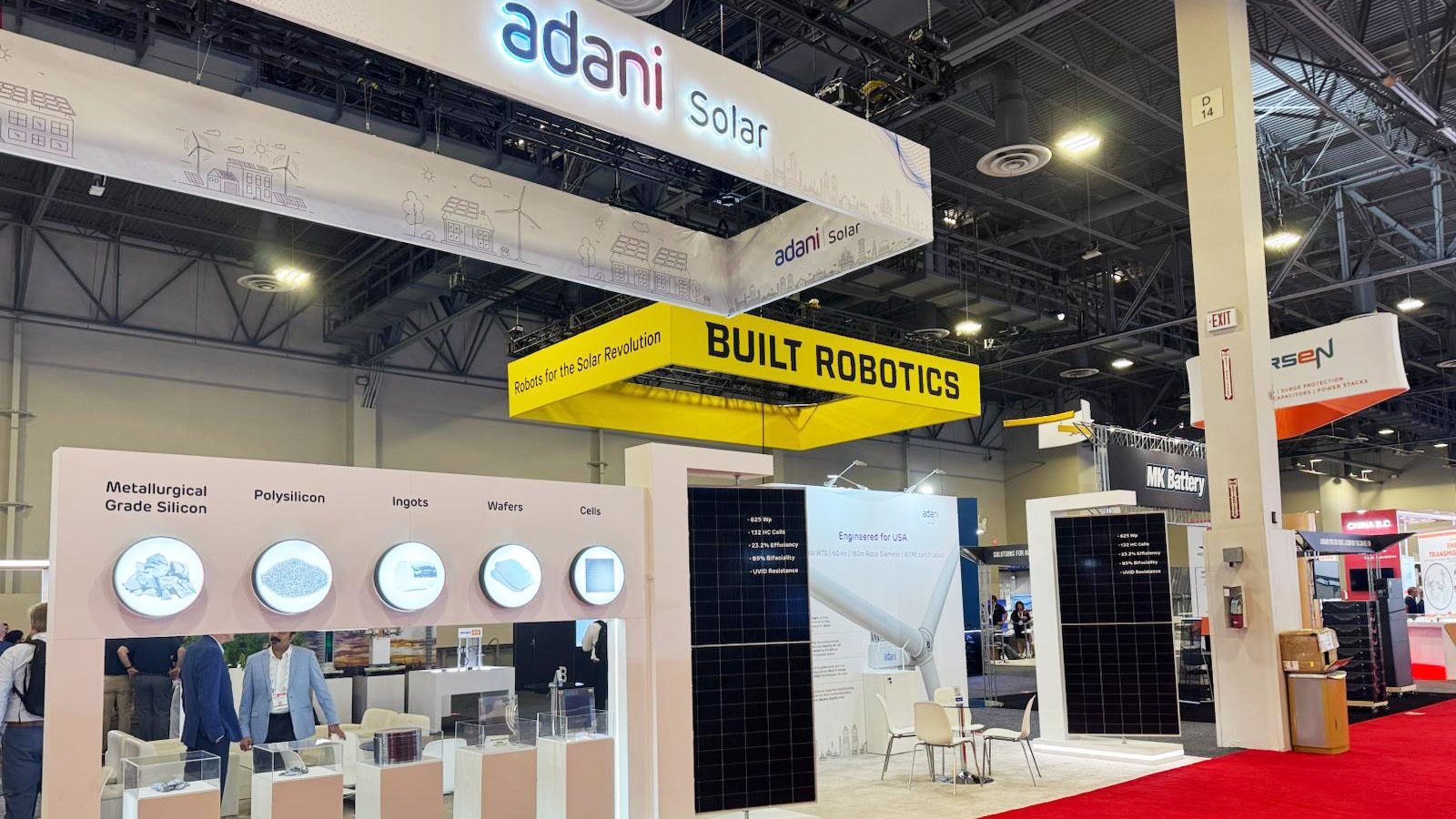 Adani Solar and Built Robotics booths at a trade show, displaying solar panels and components.