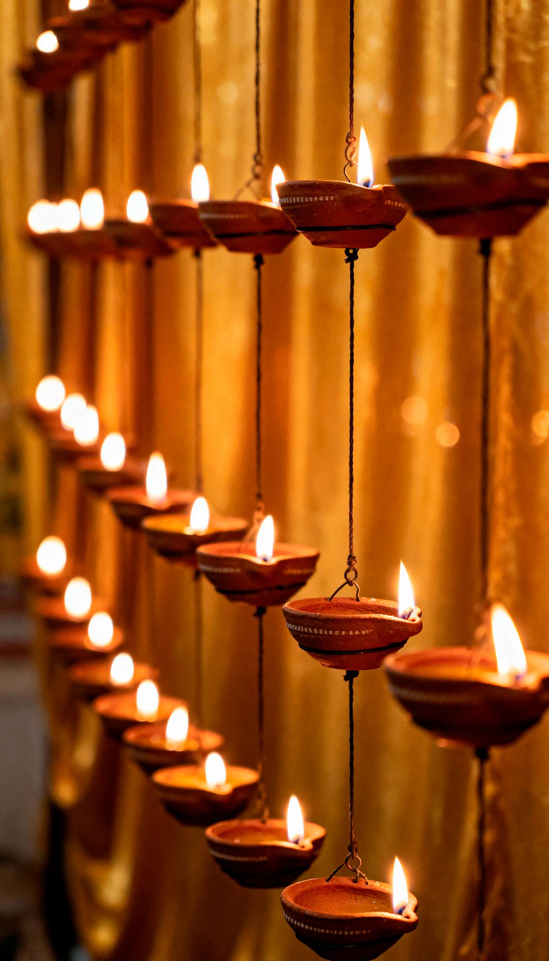 Lit clay diyas hanging in rows against a warm golden background.