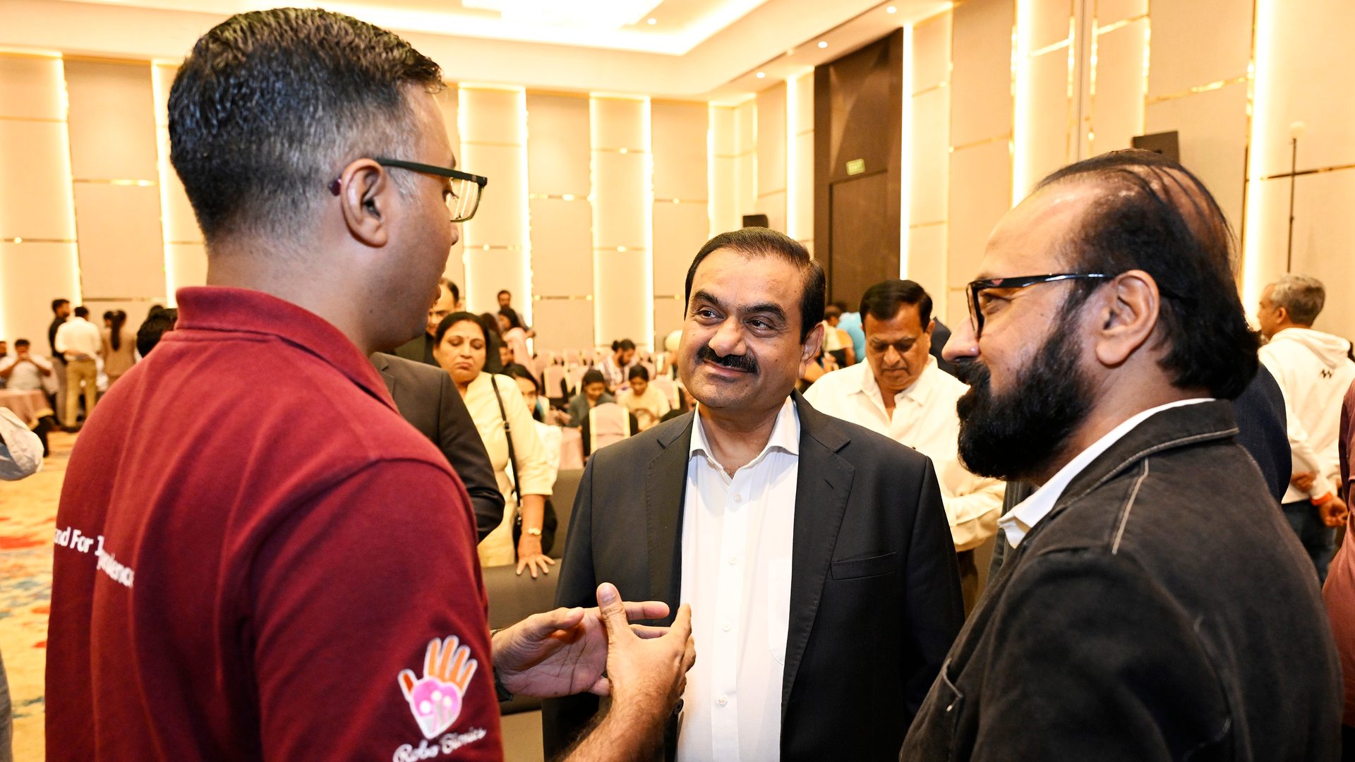 Gautam Adani smiling and conversing with two men at an indoor event.
