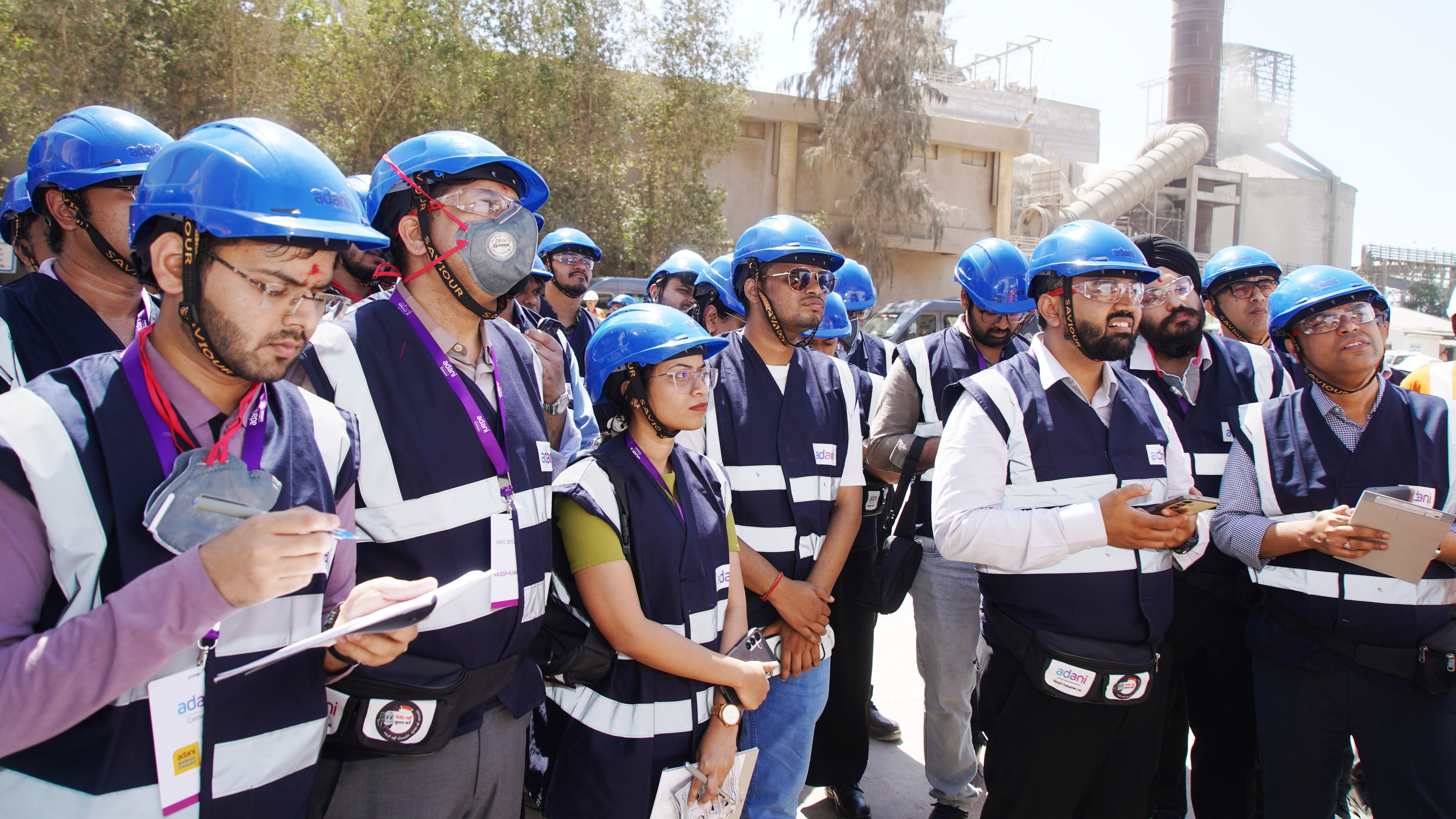 A group of Adani employees in hard hats and safety vests inspect an industrial site.