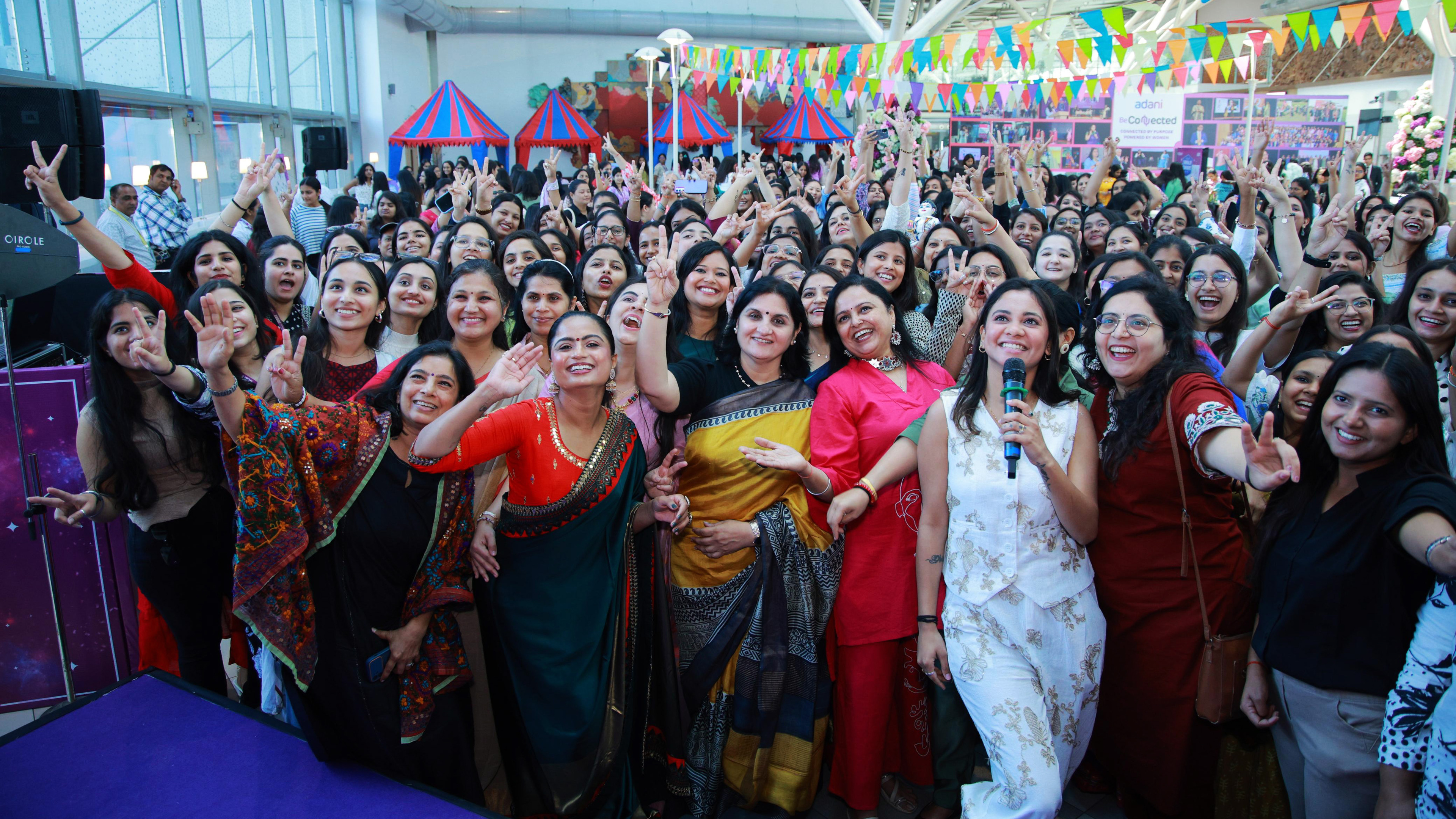 A large group of joyful women celebrating, smiling and making peace signs, likely at an event.
