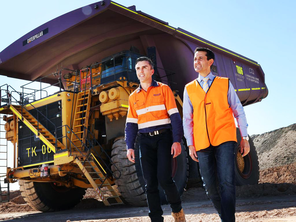 Two men in hi-vis gear walk past a giant yellow Caterpillar mining truck at a mine.