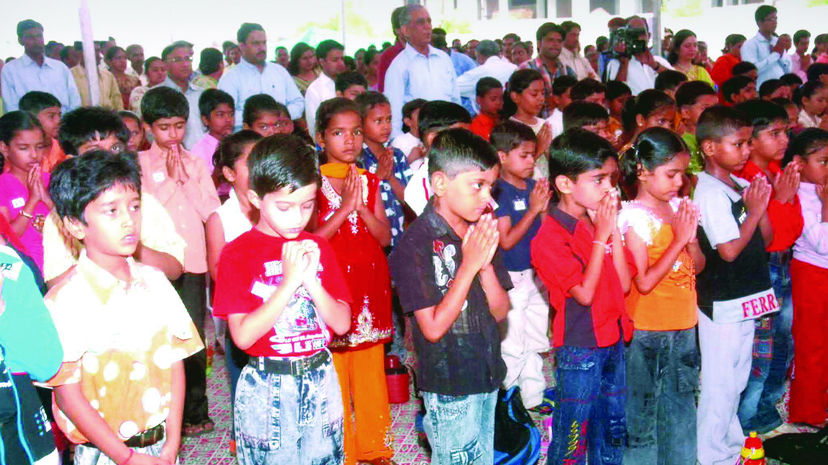 A large group of young children, predominantly boys, standing with hands folded in a prayer-like pose.