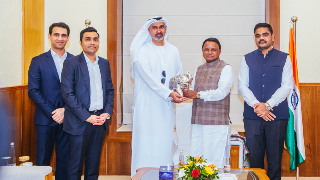 Five men, including one in traditional Arab attire, are gathered, with two exchanging a silver falcon statue.