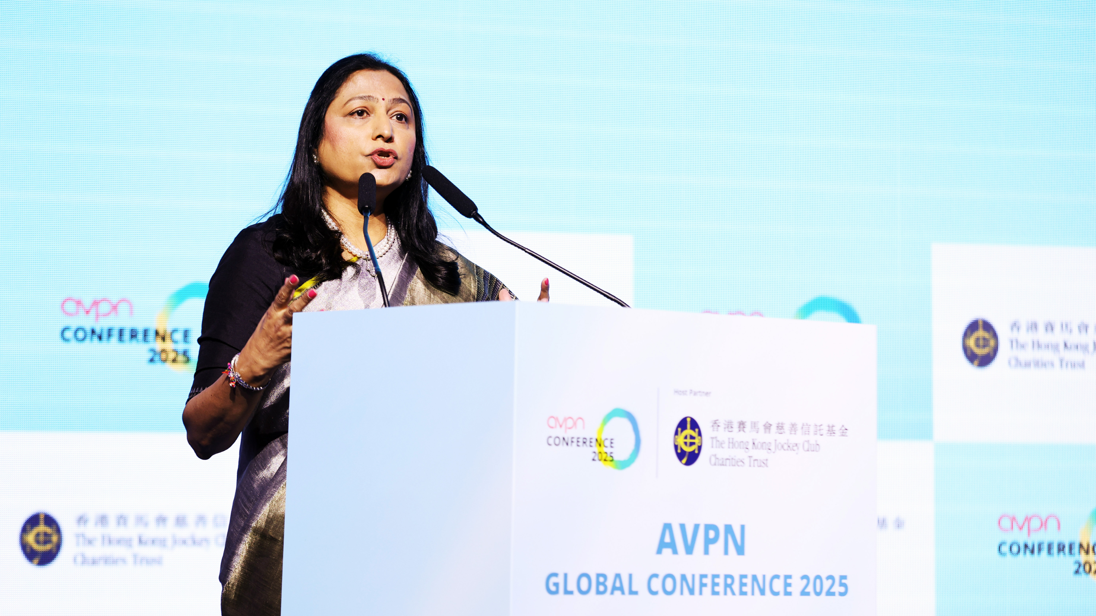 Woman speaks at AVPN Global Conference 2025, gesturing from a podium with logos visible.