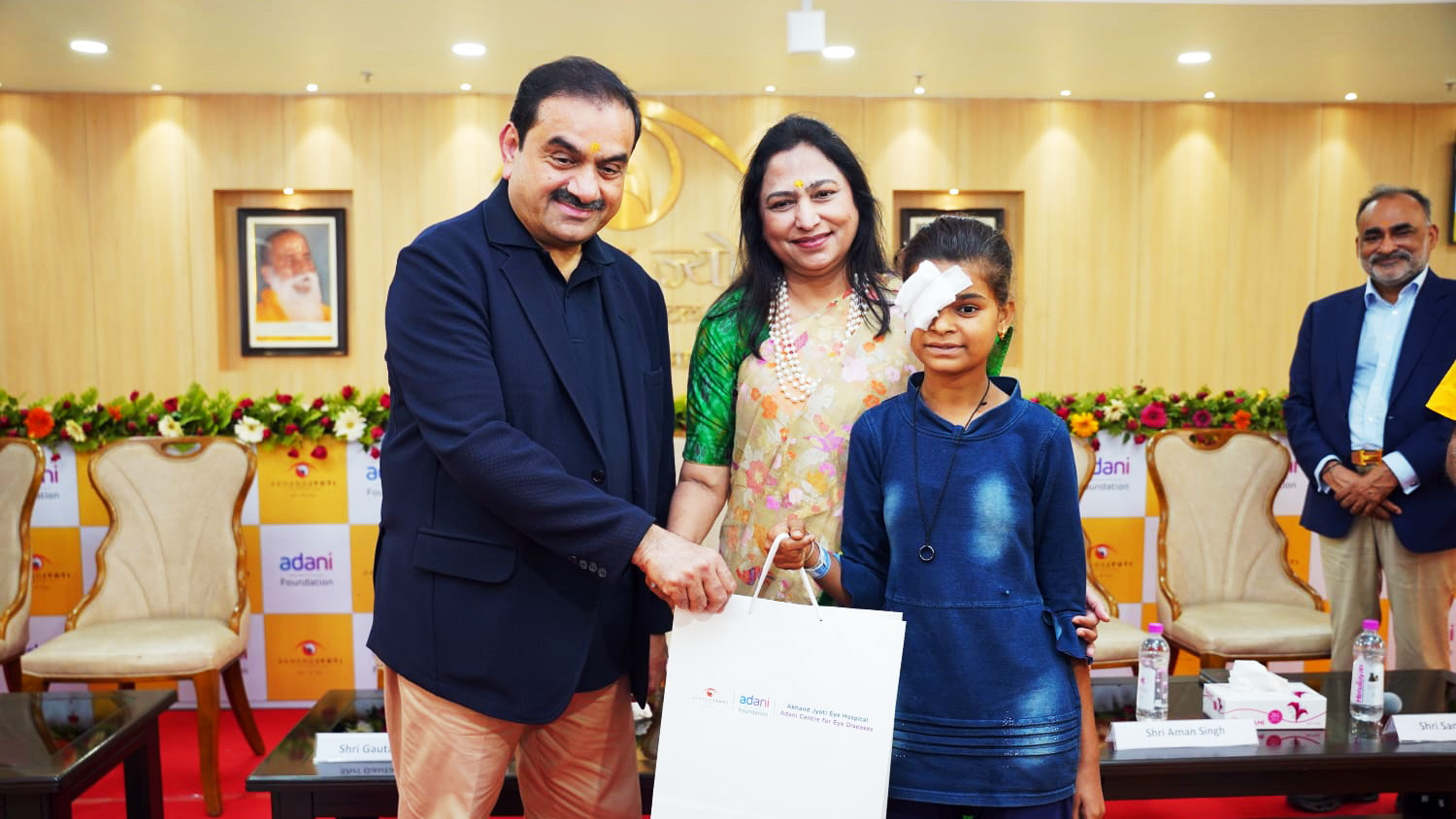 Gautam Adani and Priti Adani present a gift to a young girl with an eye patch at an eye care event.