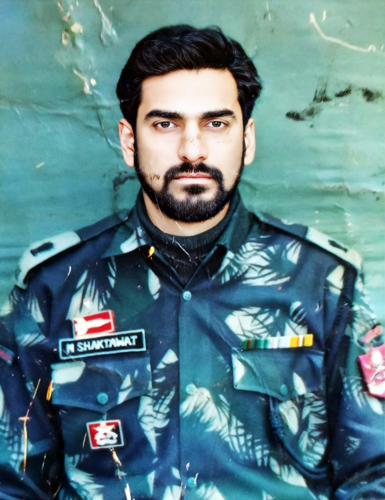 Close-up portrait of a man with a beard in a military camouflage uniform, nametag 'N SHAKTAWAT'.