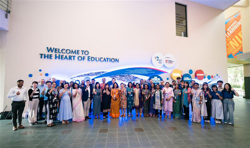 A diverse group of people posing and giving thumbs up in an atrium with a large "Welcome to the Heart of Education" sign.