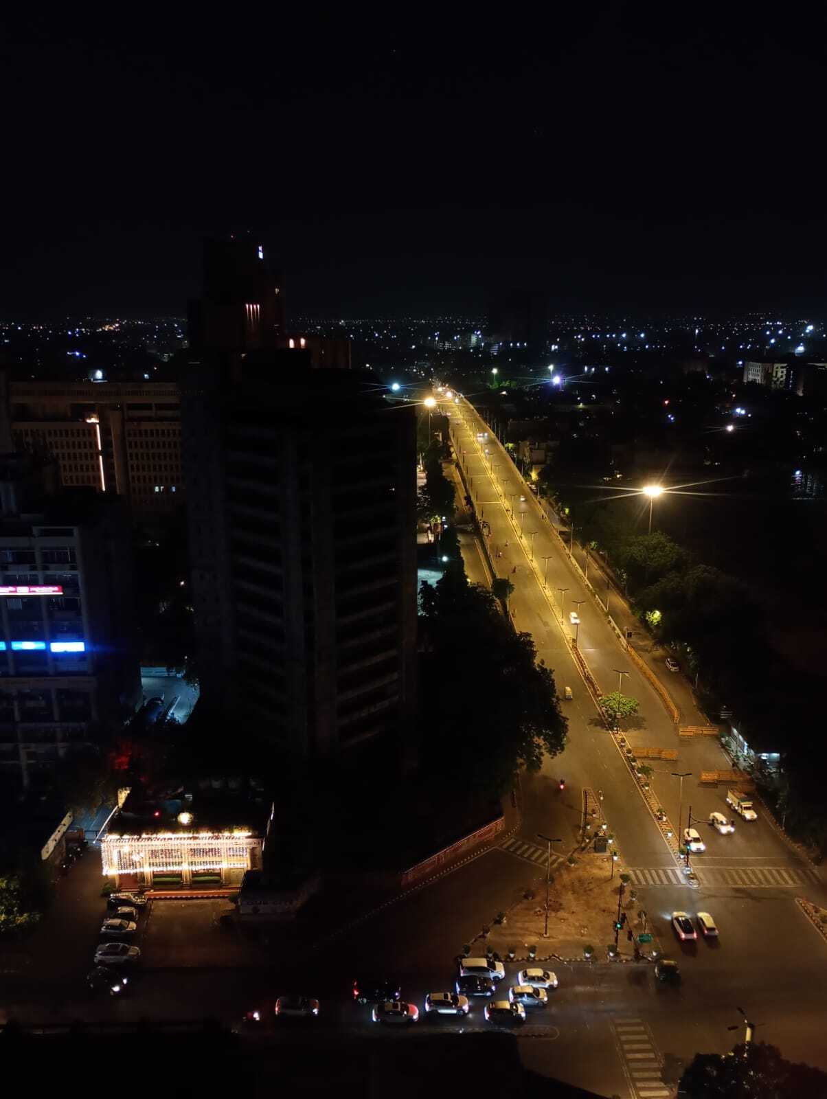 An aerial night view of a city street and an illuminated bridge, with buildings and cars visible below.