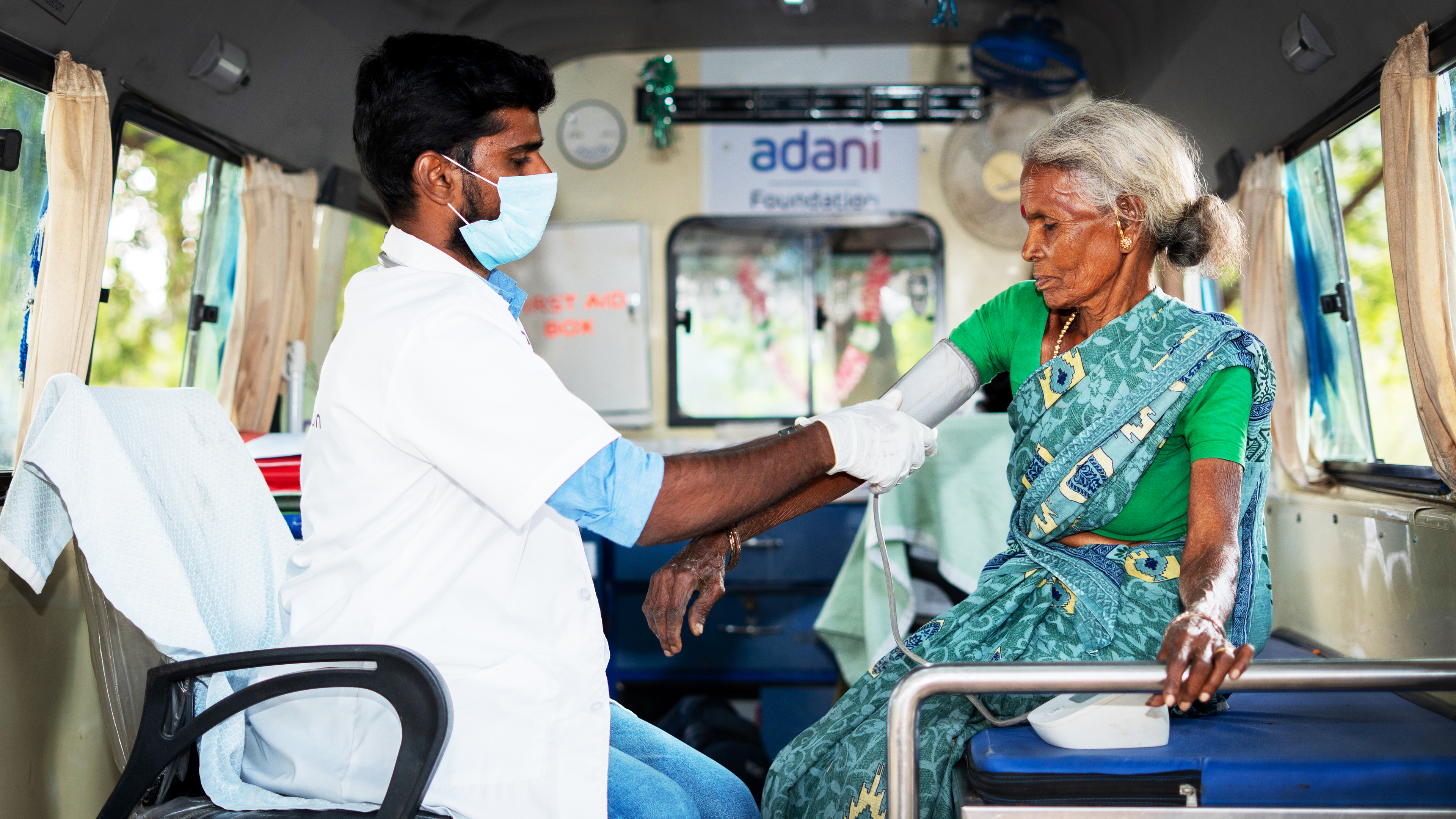 A doctor in a mask takes the blood pressure of an elderly woman in a mobile Adani Foundation clinic.