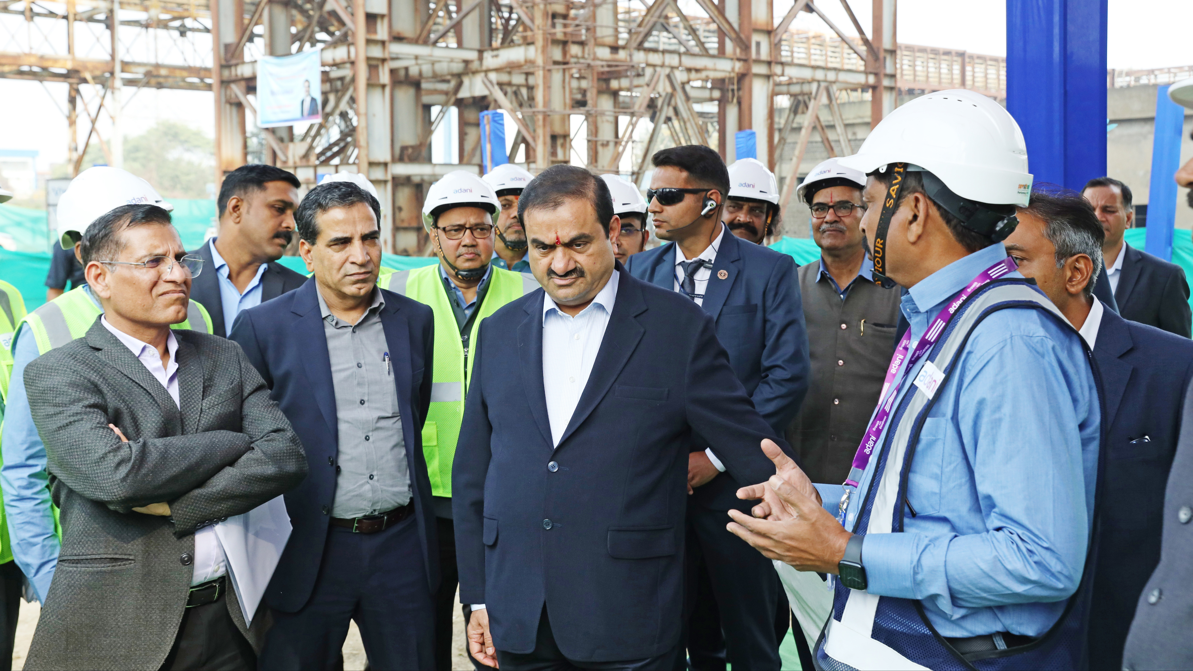 Gautam Adani and a group of executives inspecting a construction site, many wearing hard hats.
