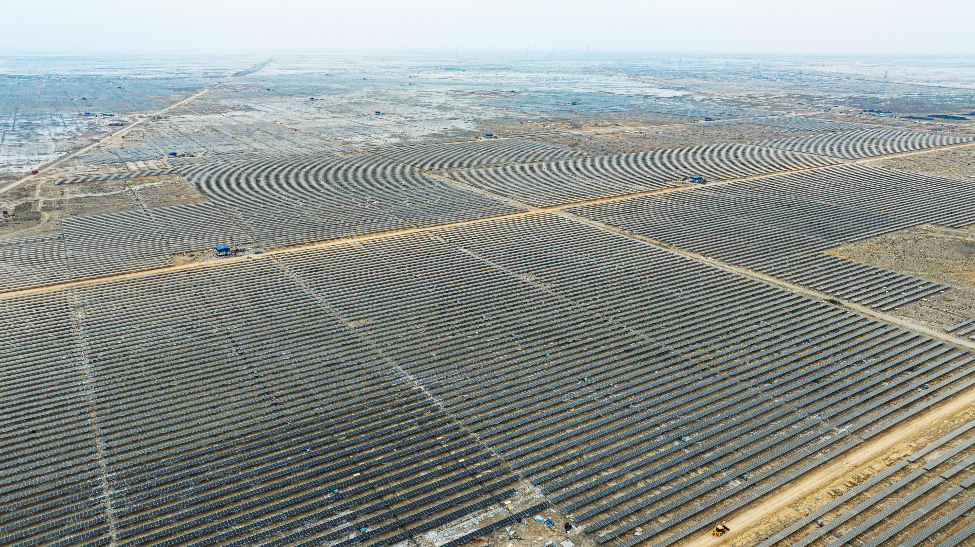 Aerial view of a massive solar farm with rows of panels stretching across a flat, arid landscape.