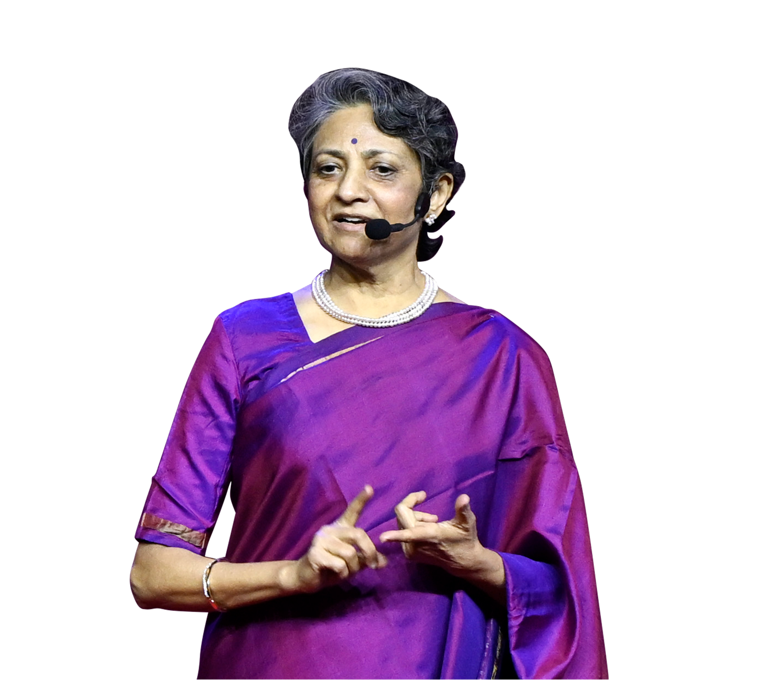 An older woman in a purple sari, pearl necklace, and headset mic, gesturing.