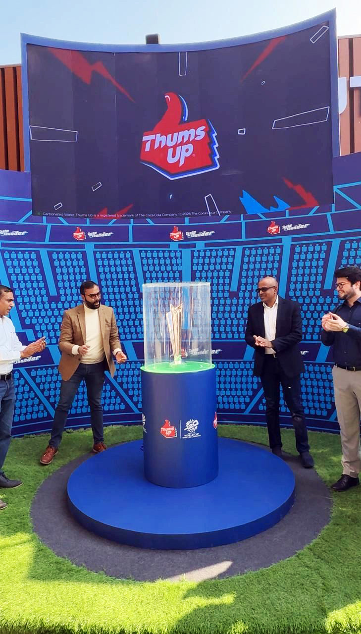 Four men gathered around a cricket trophy on display, with a large Thums Up branded screen behind them.