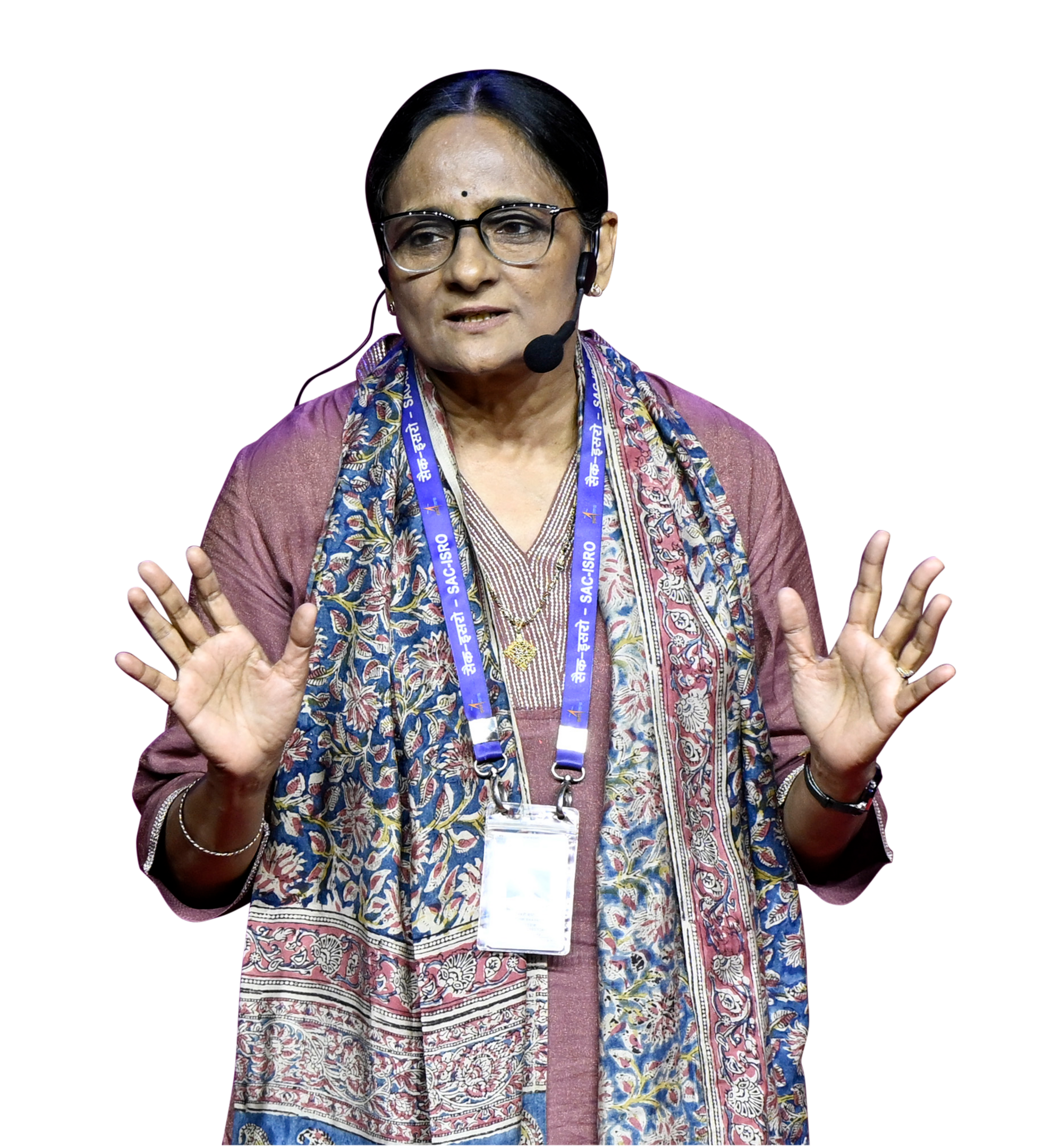 A woman in glasses and a patterned scarf speaks into a headset, gesturing with both hands.