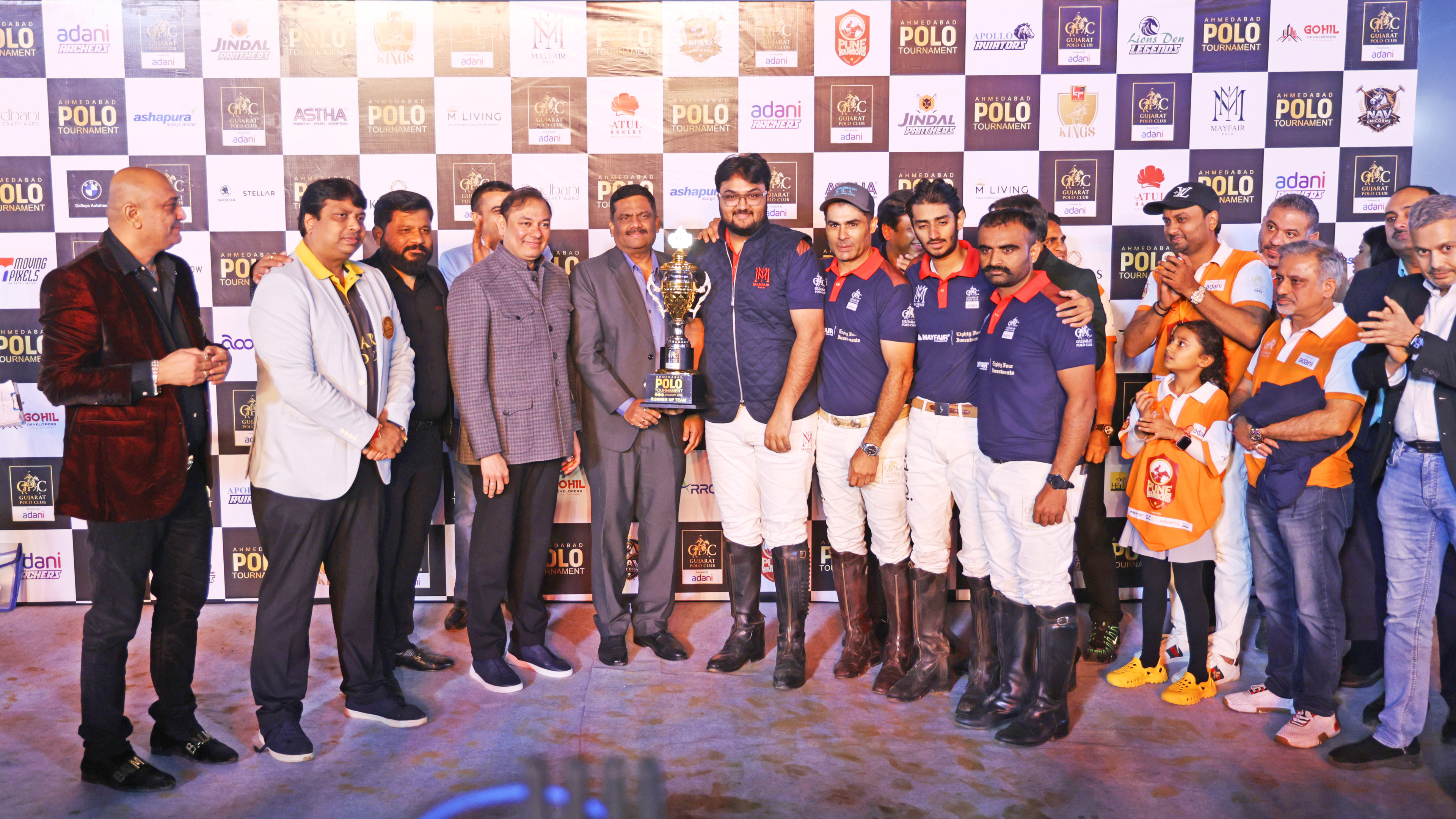 A group of men and a child, including a polo team, pose with a trophy at an event.