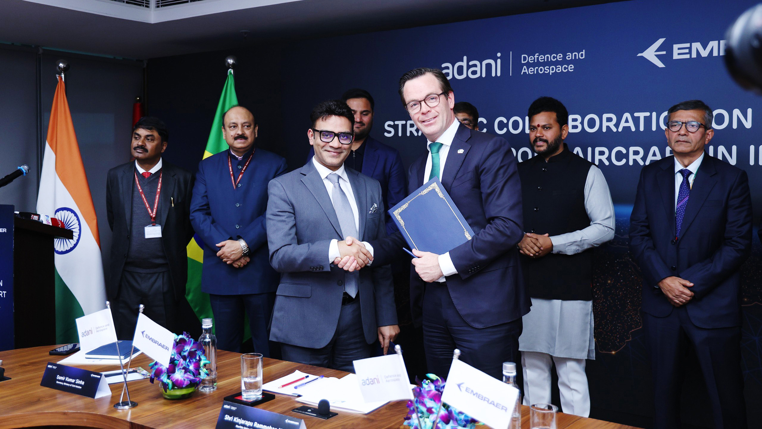 Adani and Embraer executives shake hands, symbolizing strategic collaboration for aircraft in India.