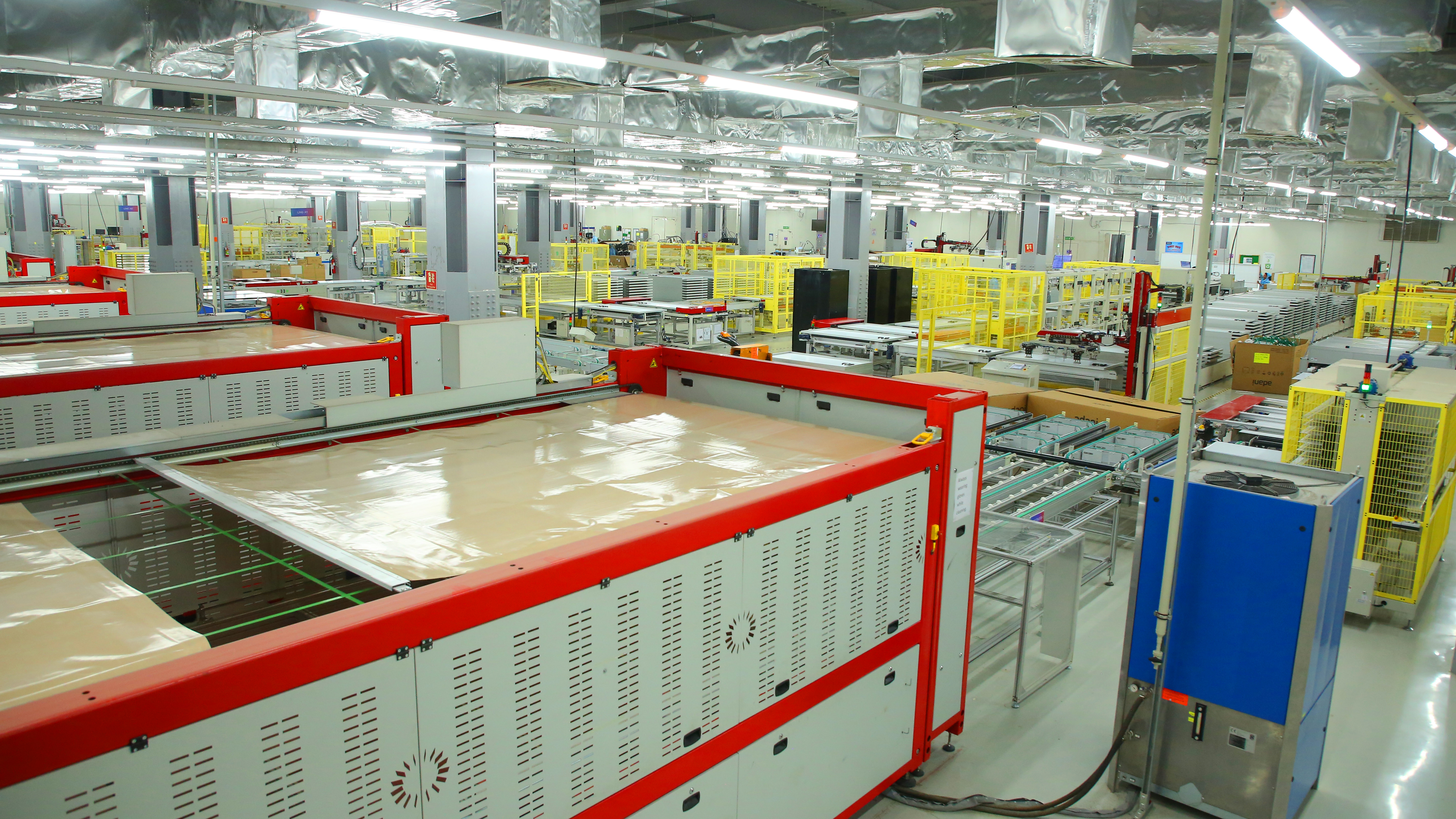 Bright, industrial factory floor with multiple production machines and safety barriers.