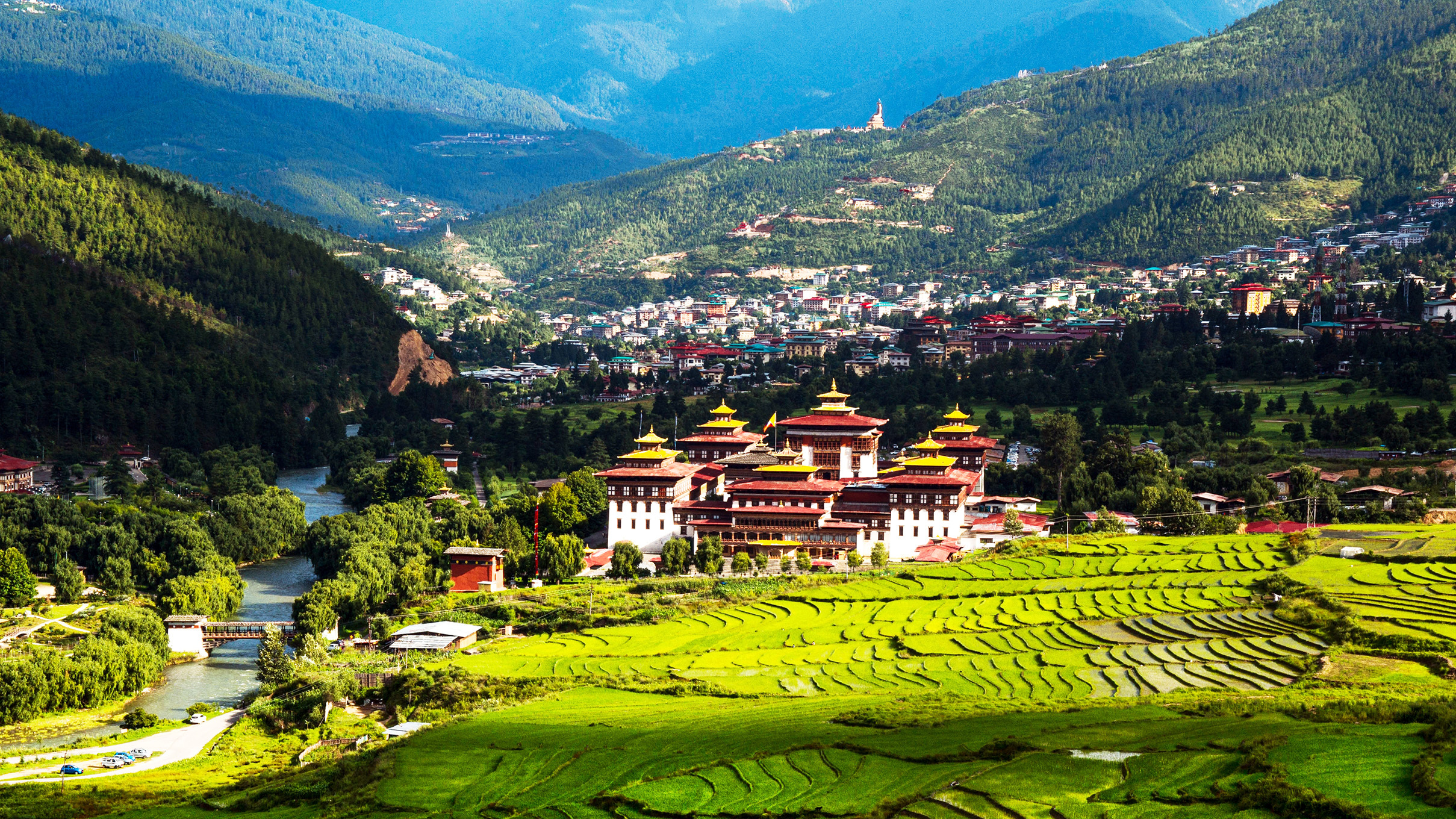 Bhutanese dzong, terraced rice fields, river, and town in a mountain valley.