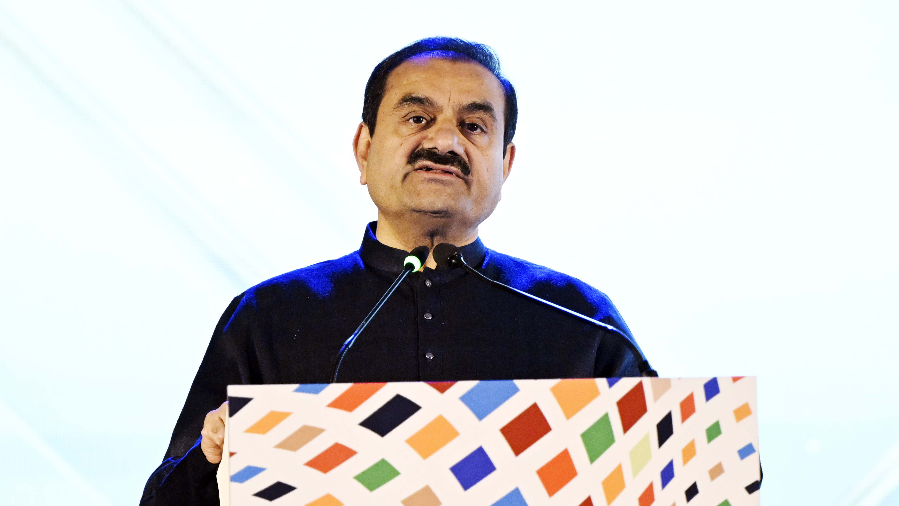 Gautam Adani speaks at a podium with microphones.