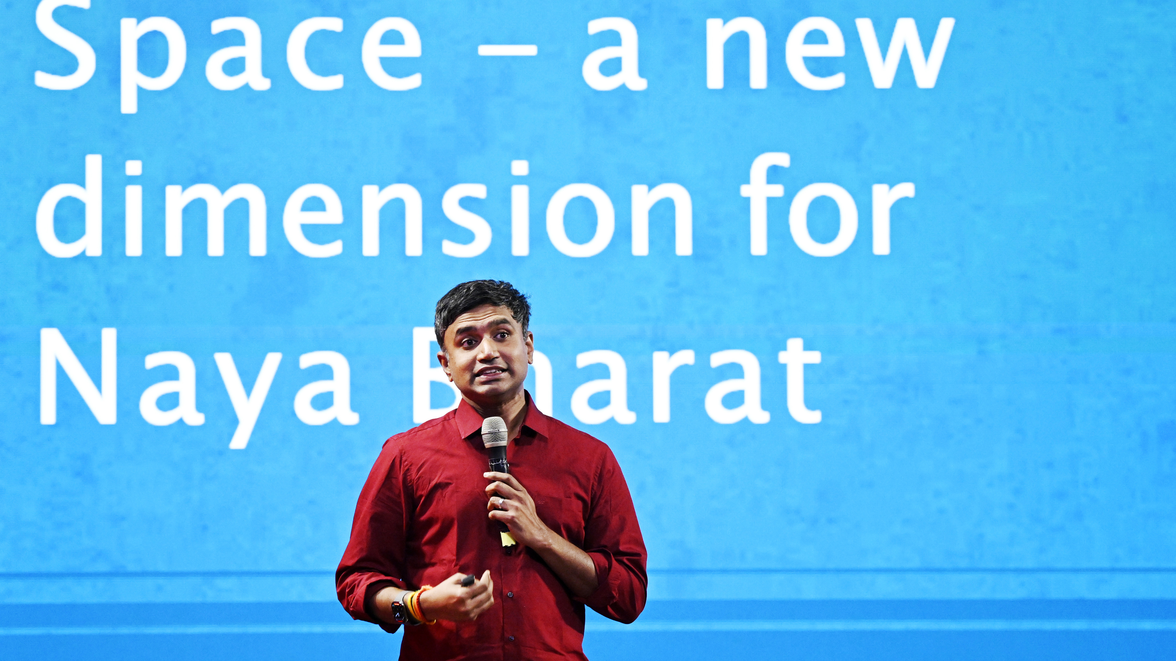 Man in red shirt speaks into mic; blue screen reads "Space - a new dimension for Naya Bharat."