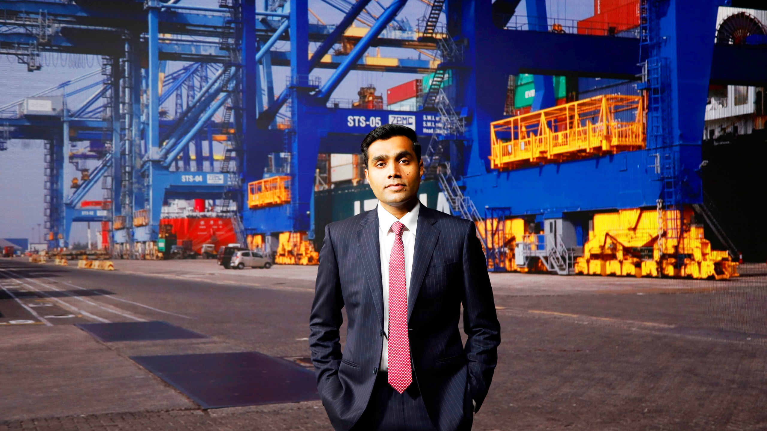Businessman at a port with large cranes and shipping containers.