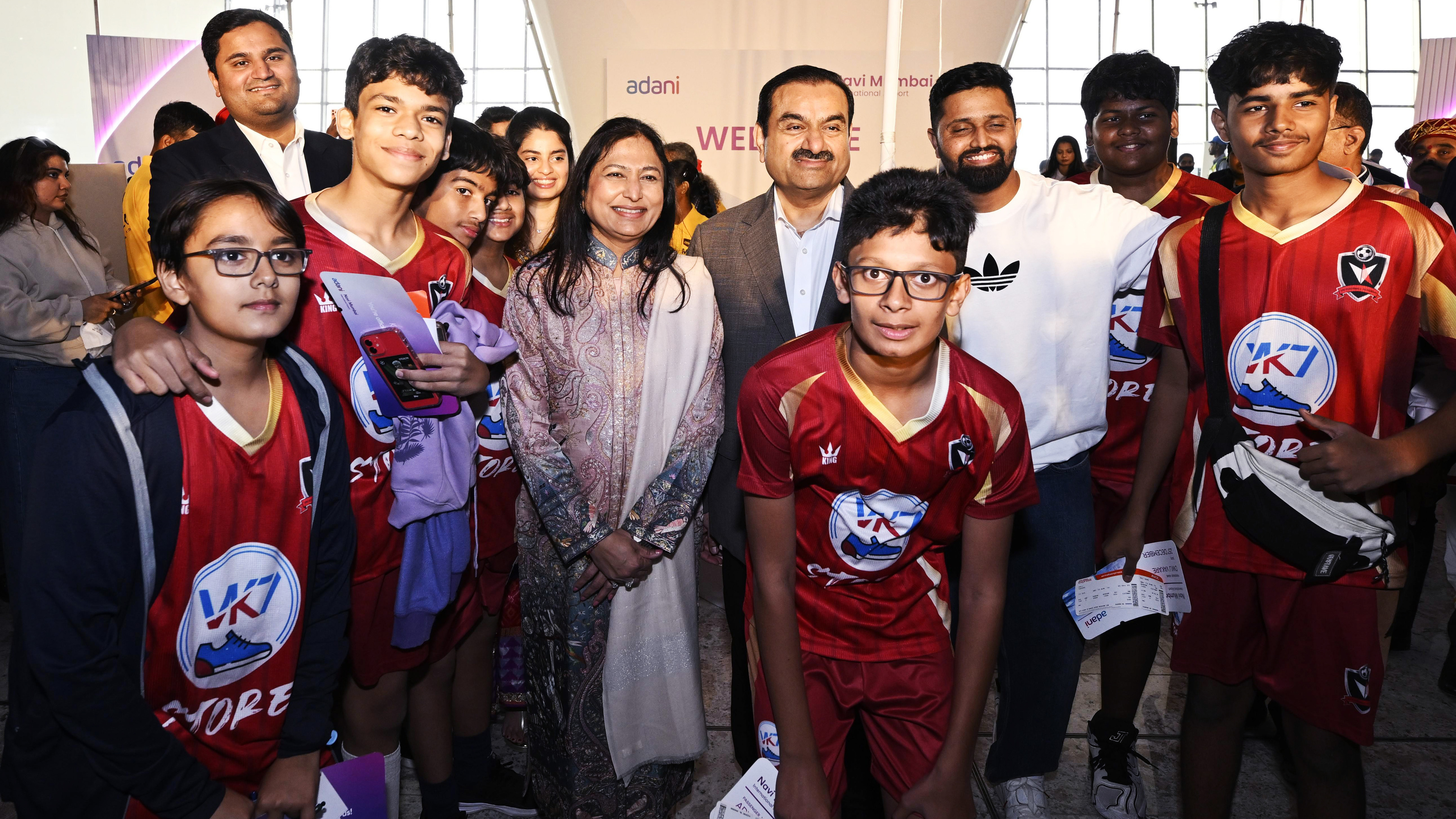 Gautam Adani and others pose with children in red sports jerseys at an Adani-sponsored event.