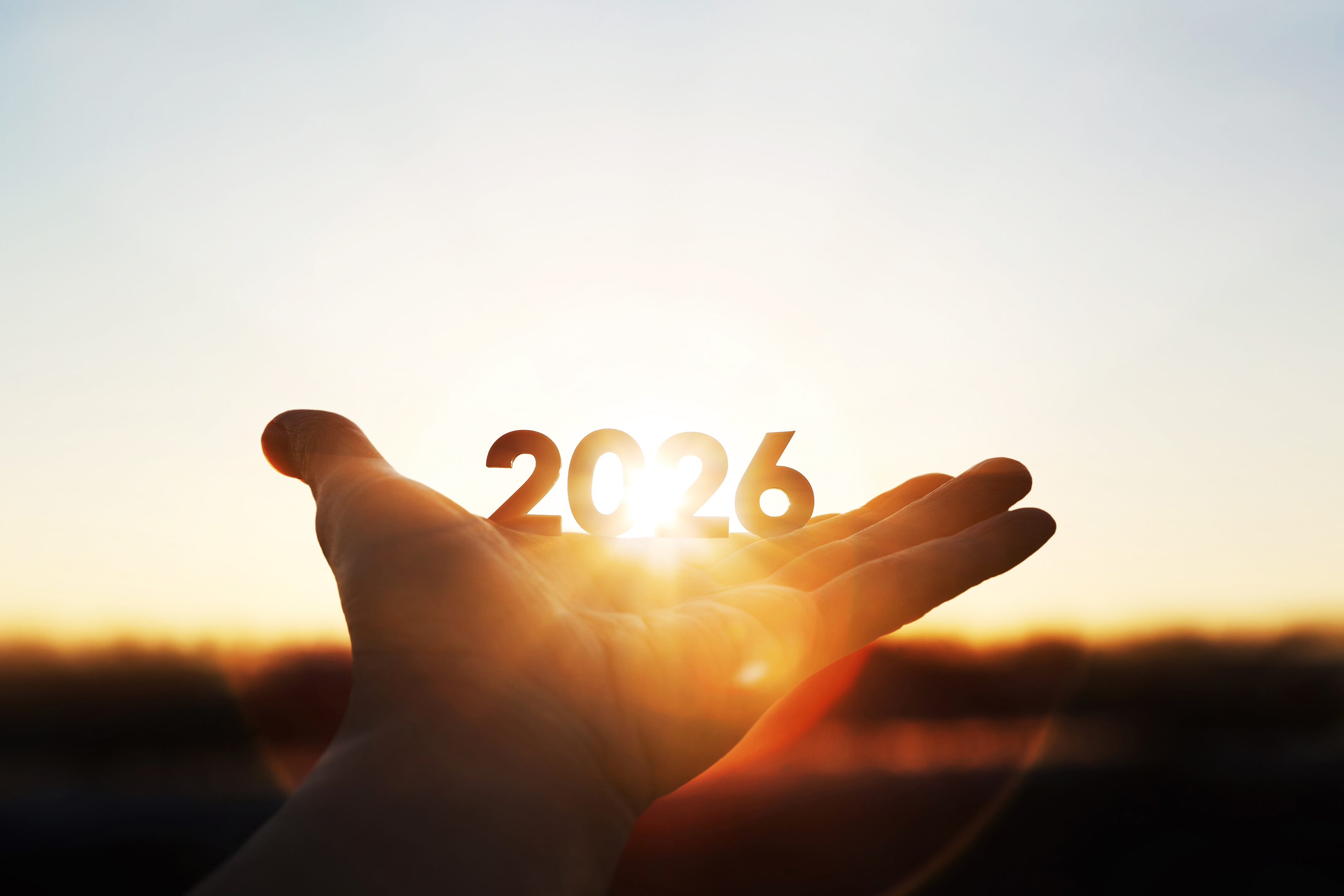 Silhouetted hand holding "2026" against a bright, sunlit sky.