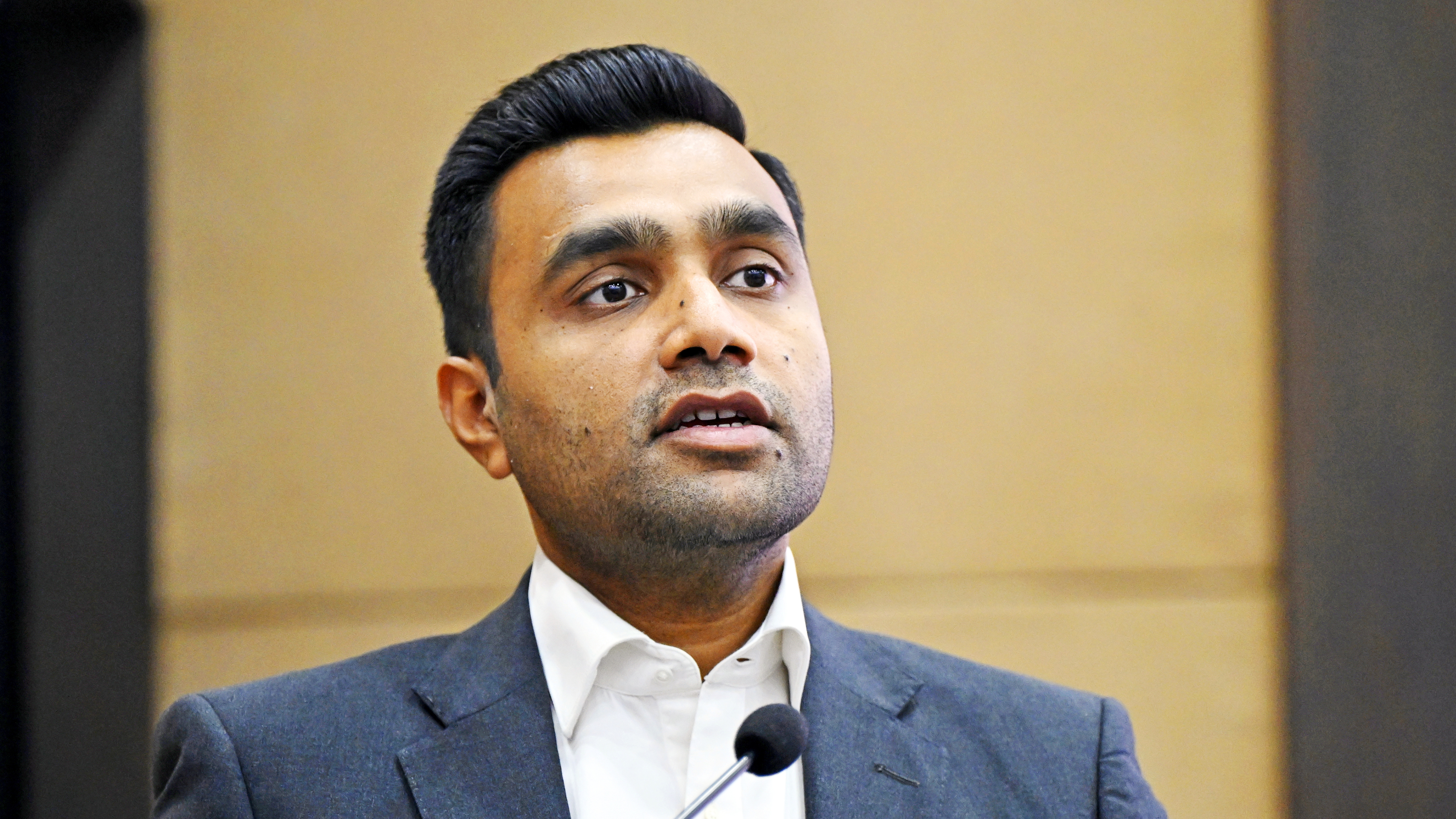 A man in a suit and white shirt speaking into a microphone.