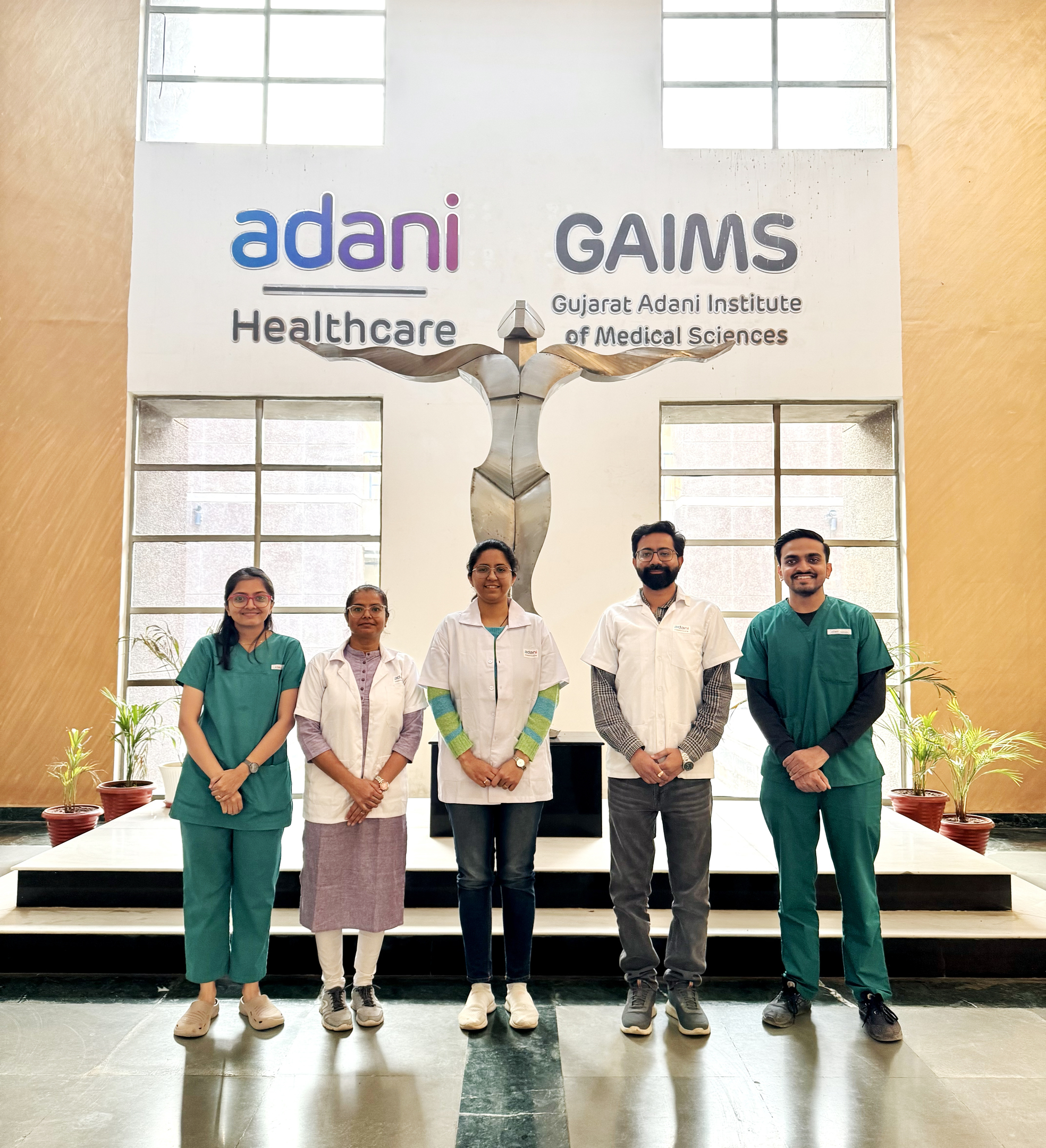 Five medical staff in front of Adani Healthcare & GAIMS logos and an abstract human sculpture.