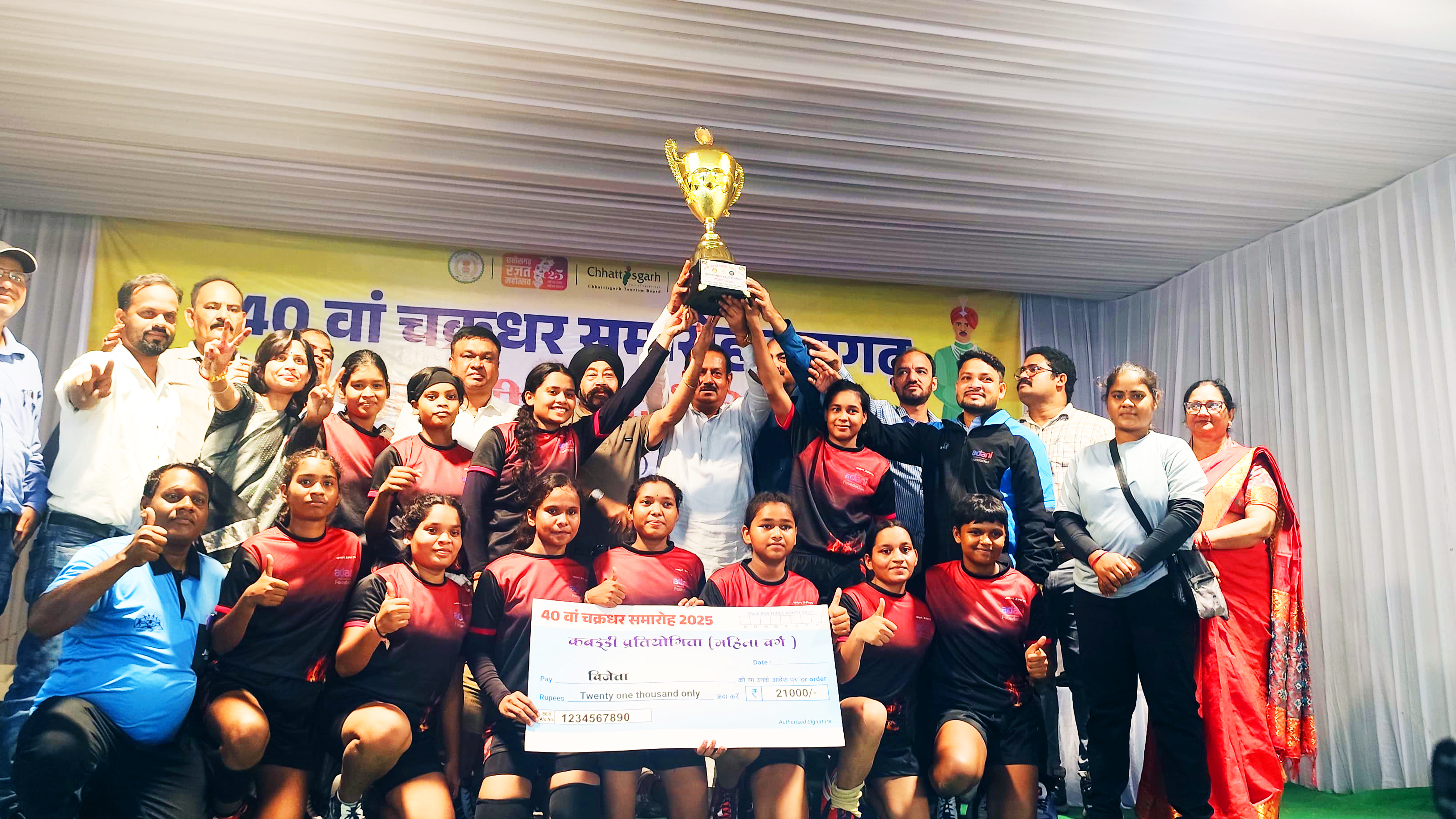 Women's kabaddi team celebrating victory with a trophy and a large prize check.